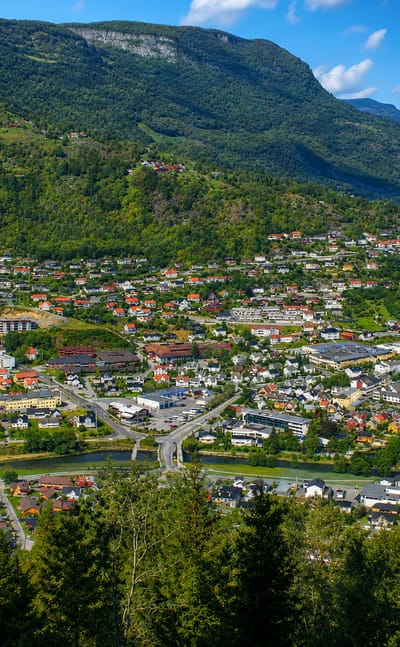 Town of Sogndalsfjora spread across a green valley beneath a steep mountain and river, Norway