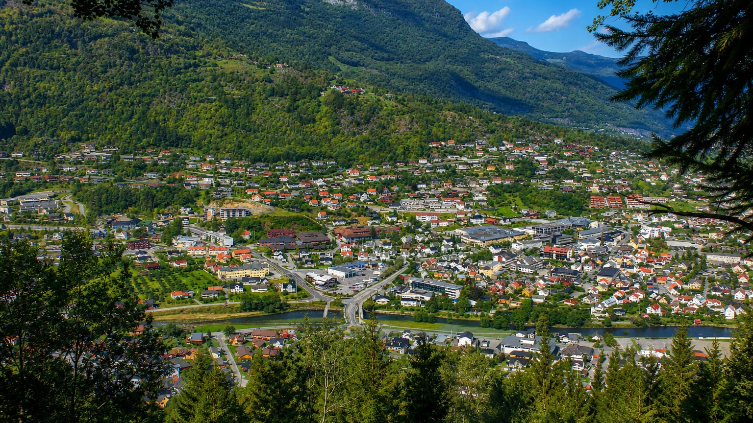 Town of Sogndalsfjora spread across a green valley beneath a steep mountain and river, Norway
