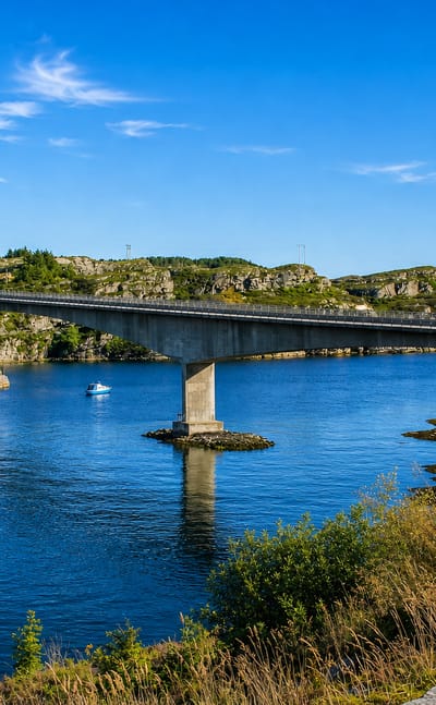 Concrete road bridge spanning blue coastal water between rocky islets near Svelgen, Norway.