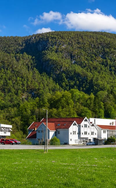 White red-roofed buildings below a forested hillside in Uggdal, Tysnes, Vestland, Norway.