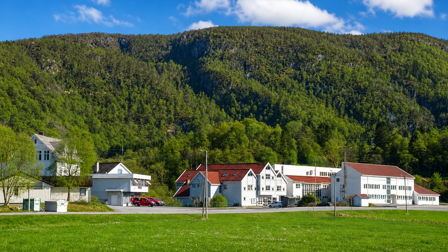 White red-roofed buildings below a forested hillside in Uggdal, Tysnes, Vestland, Norway.