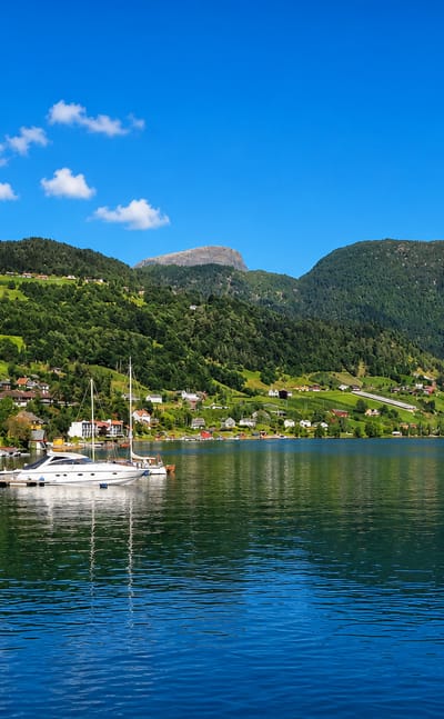 Ulvik, Norway, a waterfront village with a moored yacht and green hills rising above the Hardangerfjord.