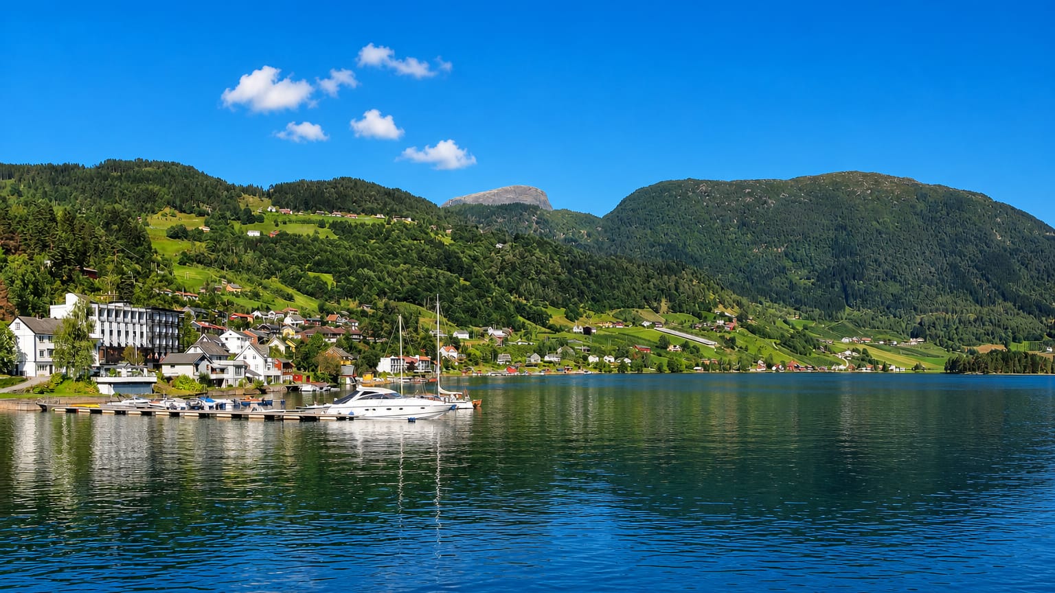 Ulvik, Norway, a waterfront village with a moored yacht and green hills rising above the Hardangerfjord.