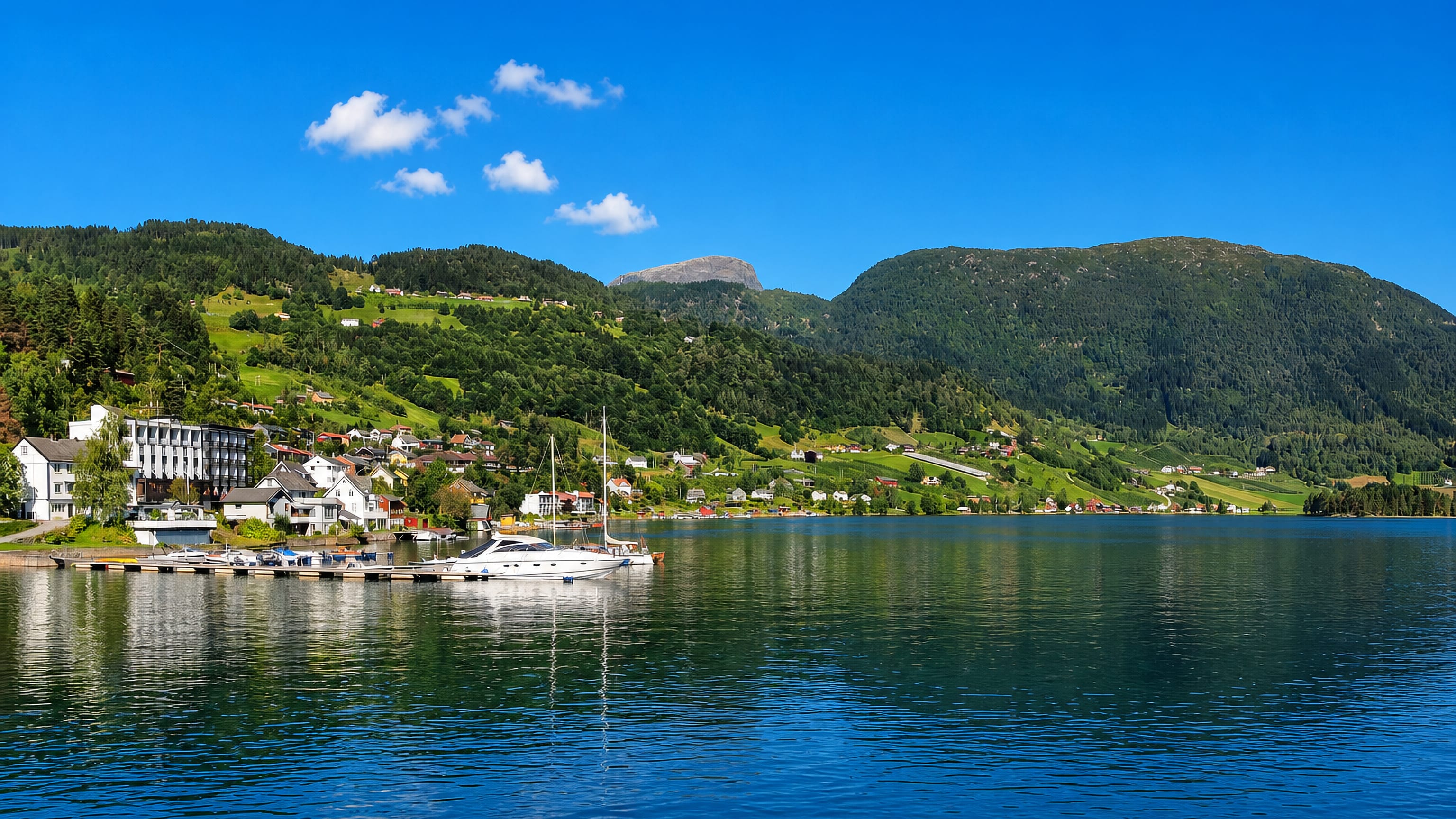 Ulvik, Norway, a waterfront village with a moored yacht and green hills rising above the Hardangerfjord.