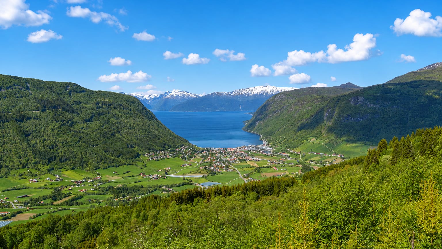 Village of Vikoyri on the green shore of the Sognefjord below snow-capped mountains, Norway