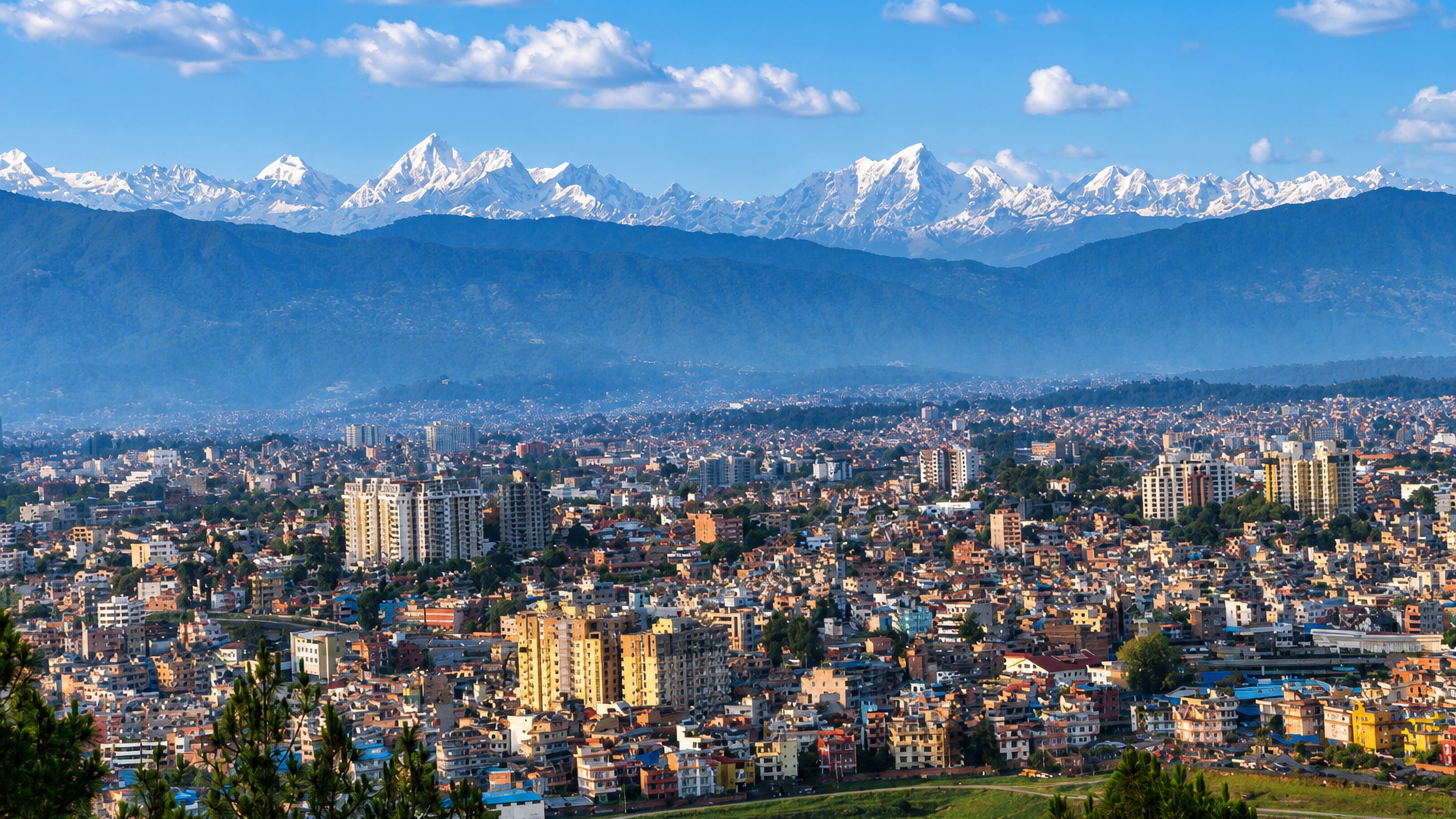 Pātan's dense Kathmandu Valley rooftops and apartment blocks below the snow-capped Himalayan range in Nepal.