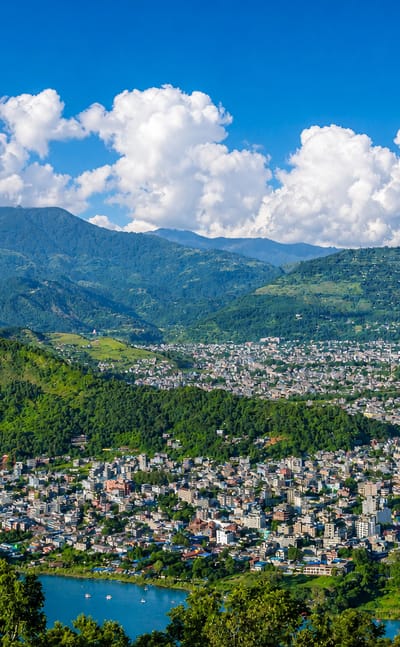 Pokhara, Nepal, spread along the shore of Phewa Lake below forested foothills and mountains.