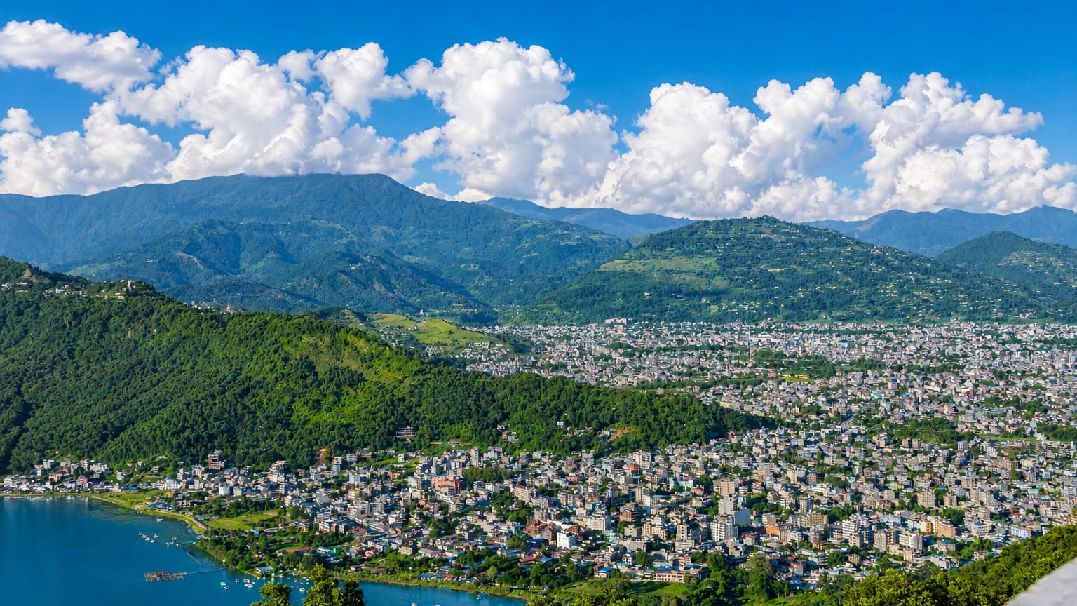 Pokhara, Nepal, spread along the shore of Phewa Lake below forested foothills and mountains.