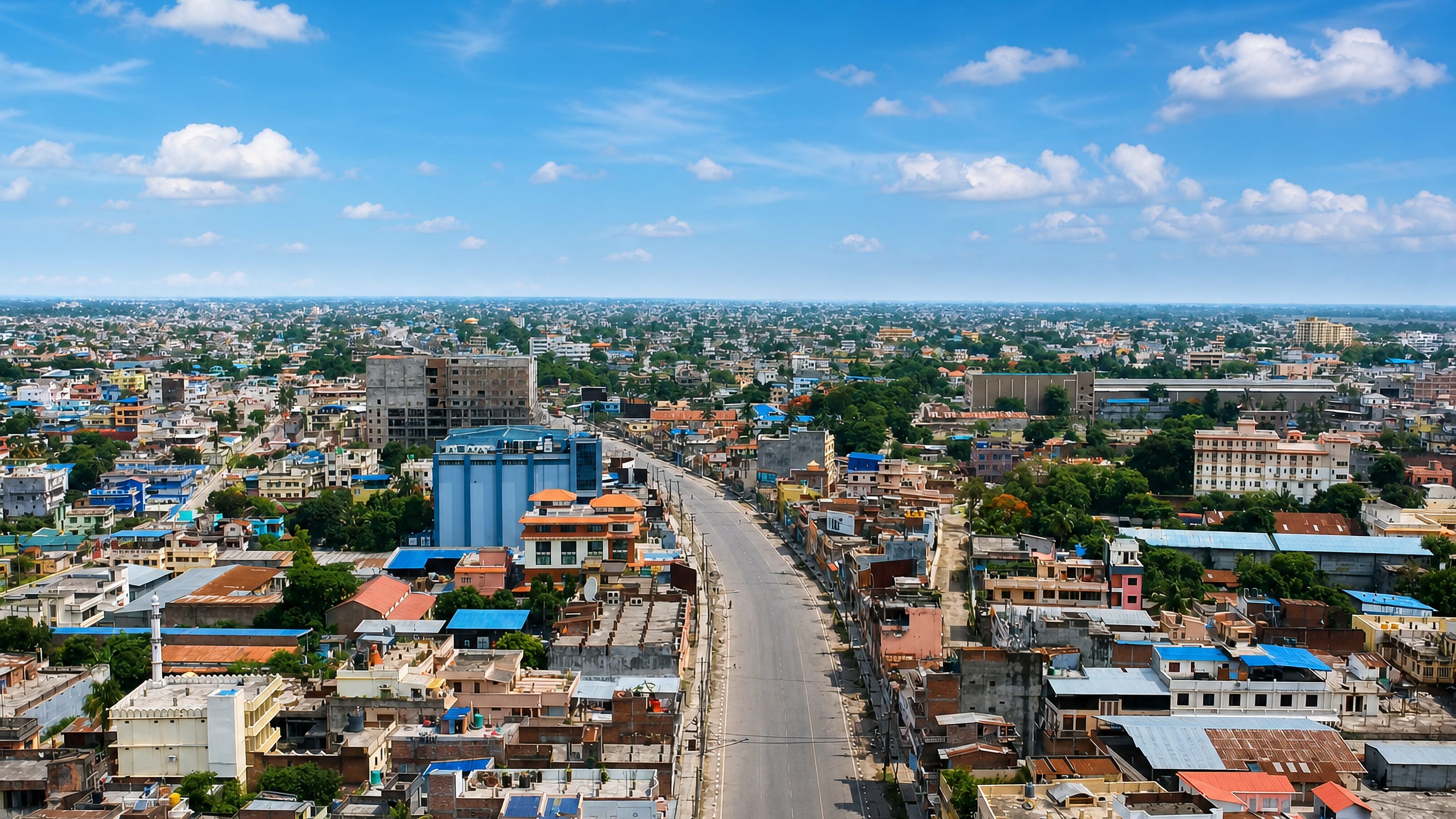 Aerial view of Biratnagar, Nepal, a broad main road cutting through dense low-rise blocks on the Terai plain.
