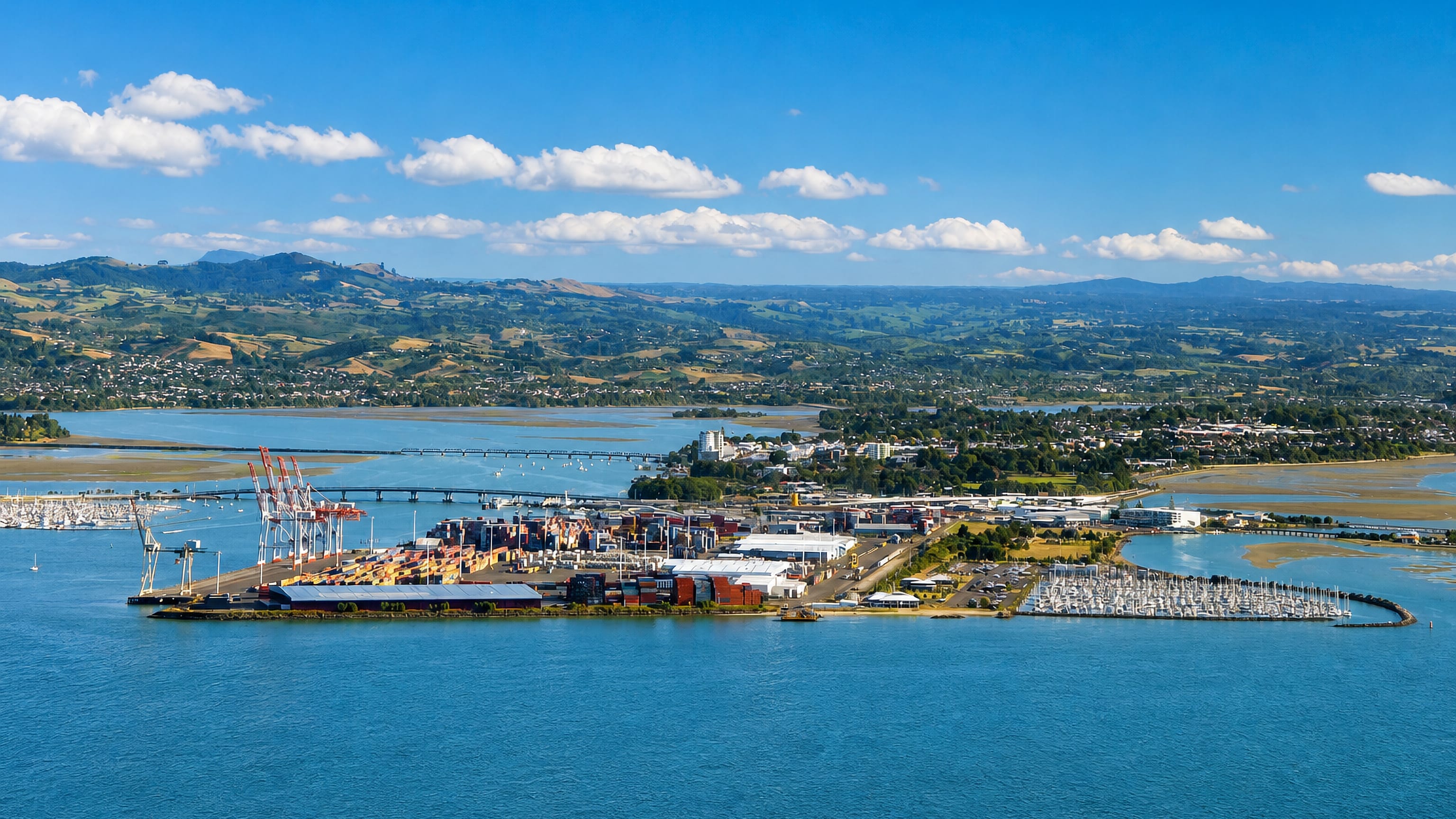 Aerial view of Tauranga harbour, New Zealand, with container port cranes, marina yachts and Bay of Plenty hills.