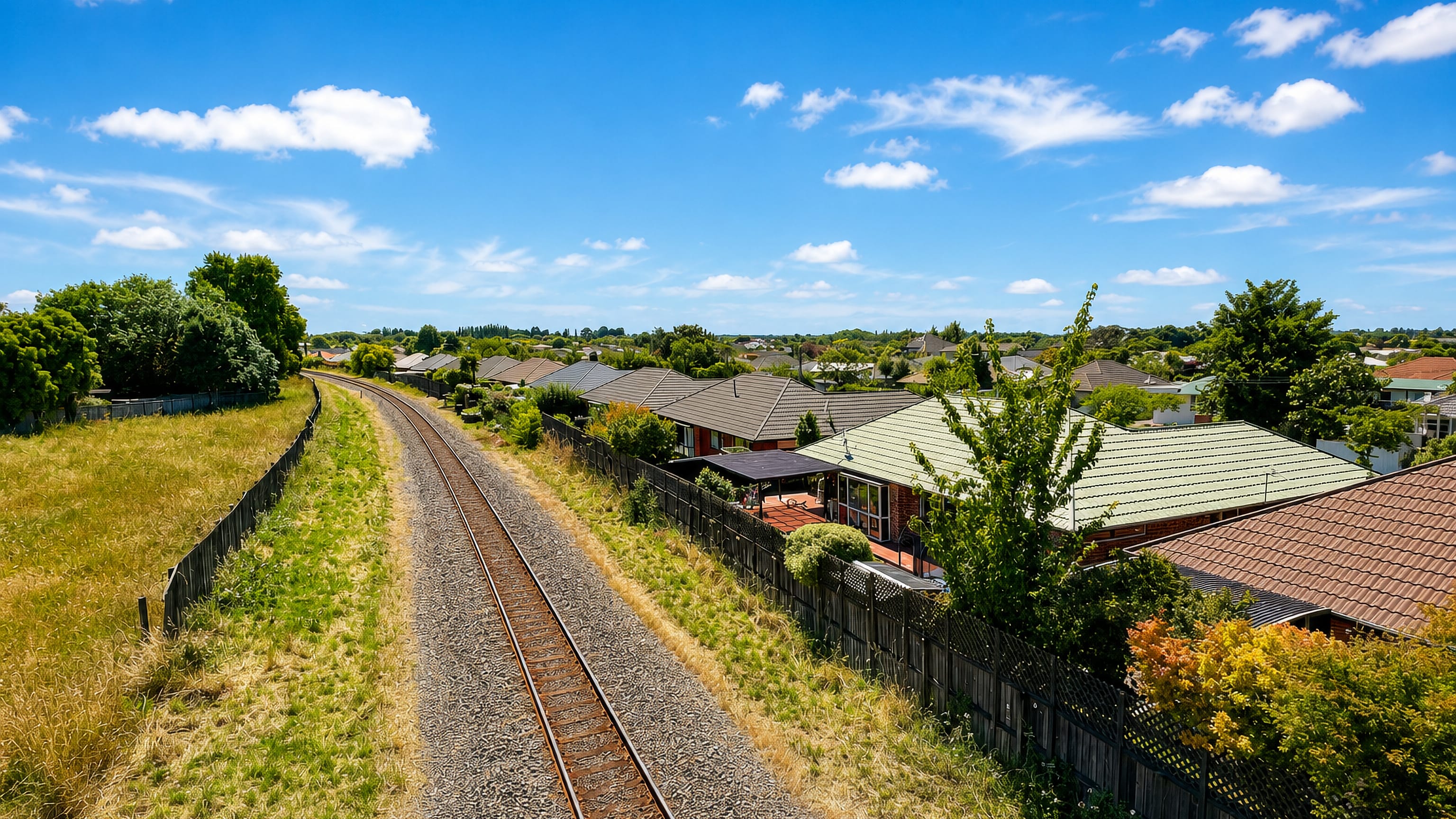 Railway line running past single-storey suburban houses under a wide blue sky in Redwood, Christchurch.