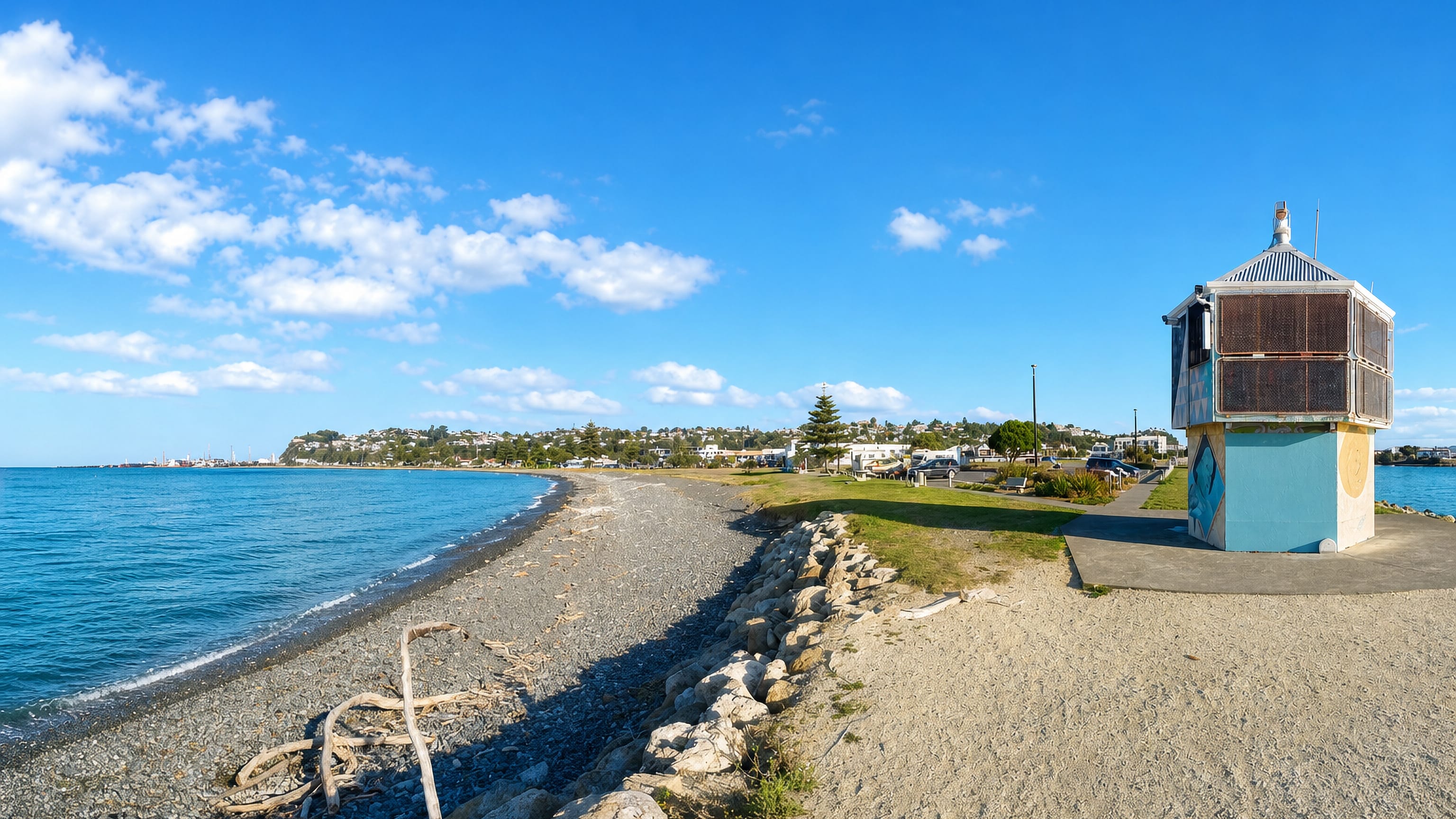Shingle beach and painted kiosk on Napier's waterfront, with the hillside suburb and port beyond