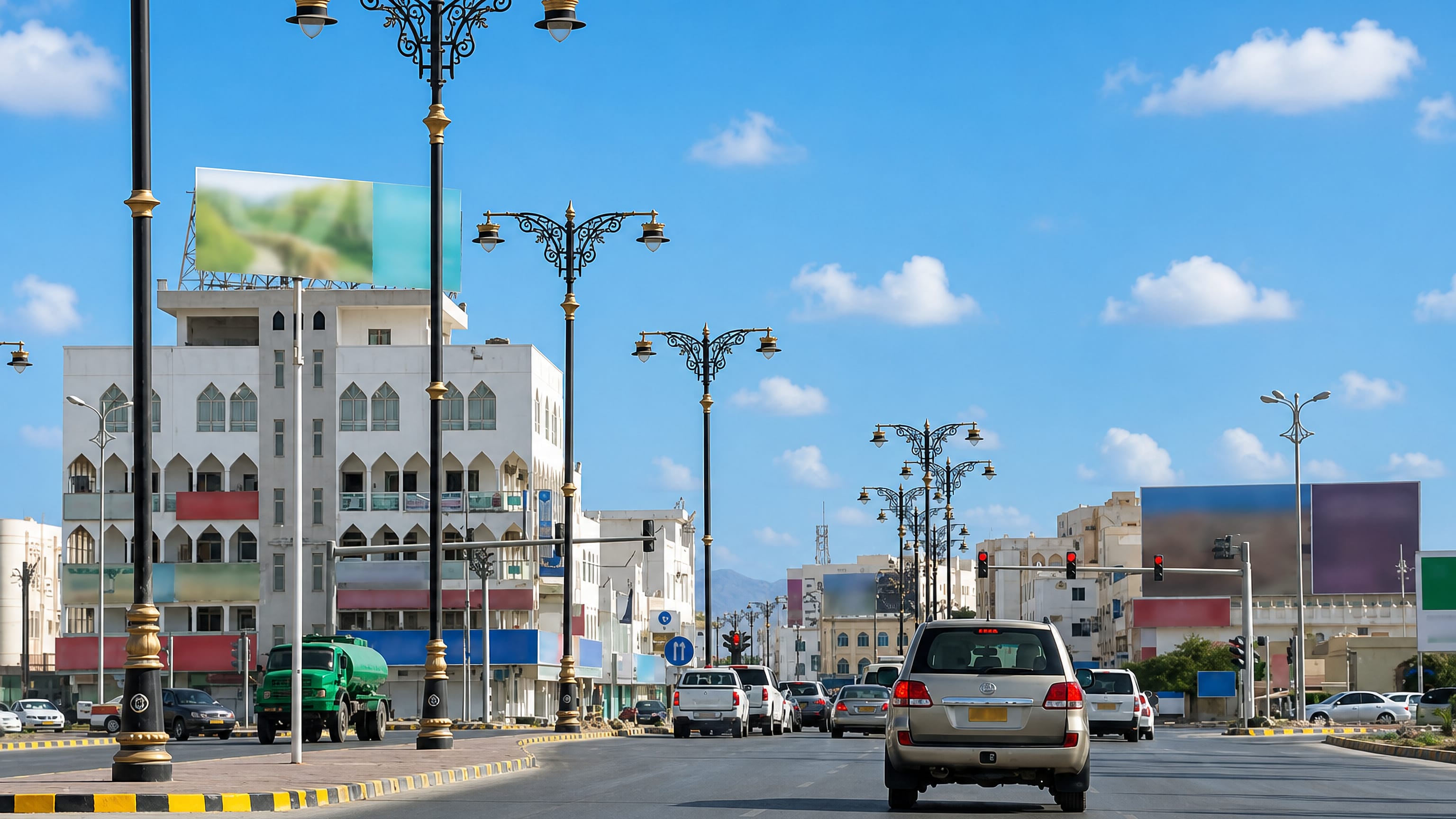 Traffic on a palm-lined boulevard in Salalah, Oman, lined with white arched buildings and ornate street lamps