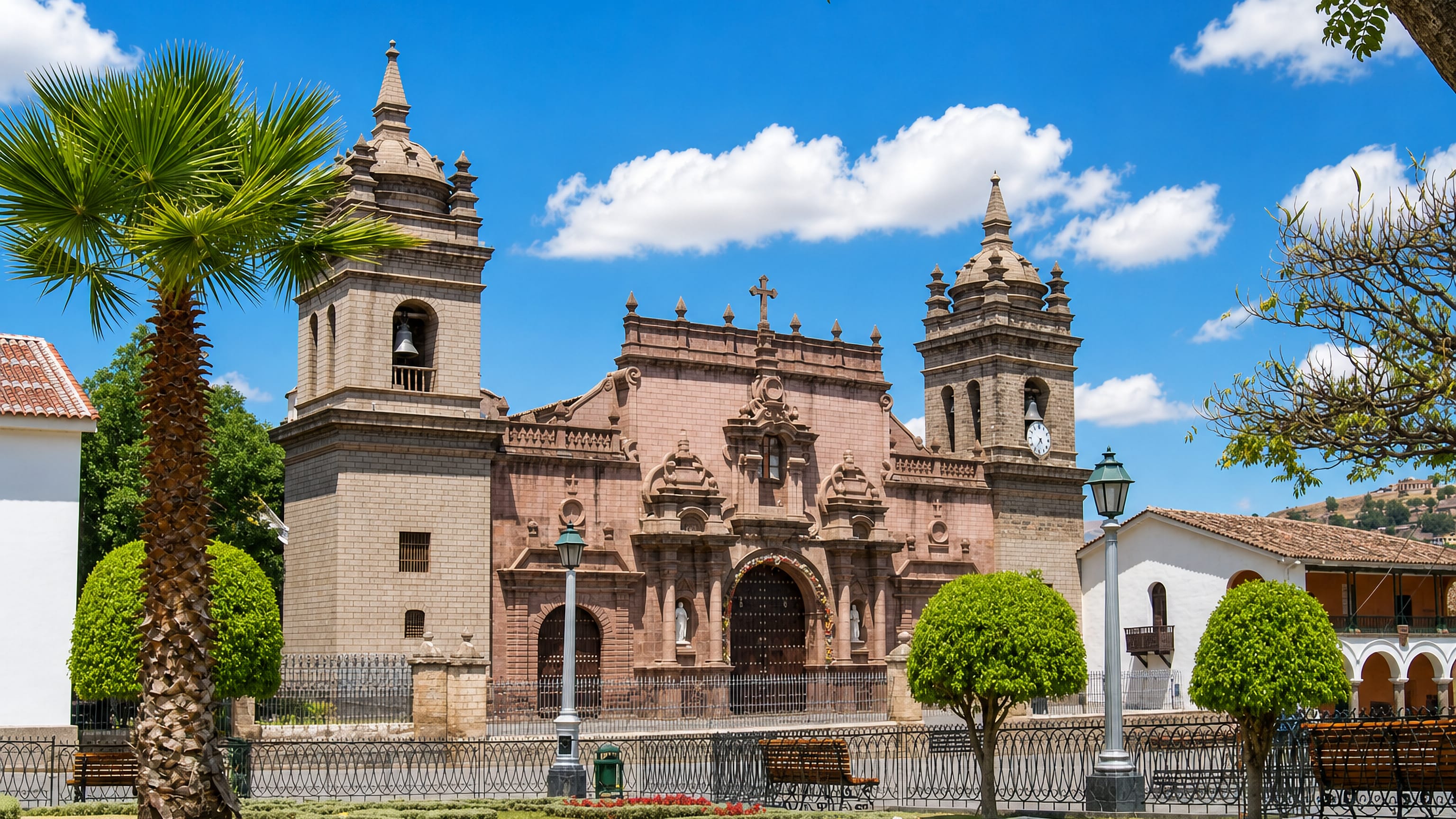 Ayacucho's pink stone cathedral with twin bell towers on the Plaza de Armas, Peru, framed by palms and flowerbeds.
