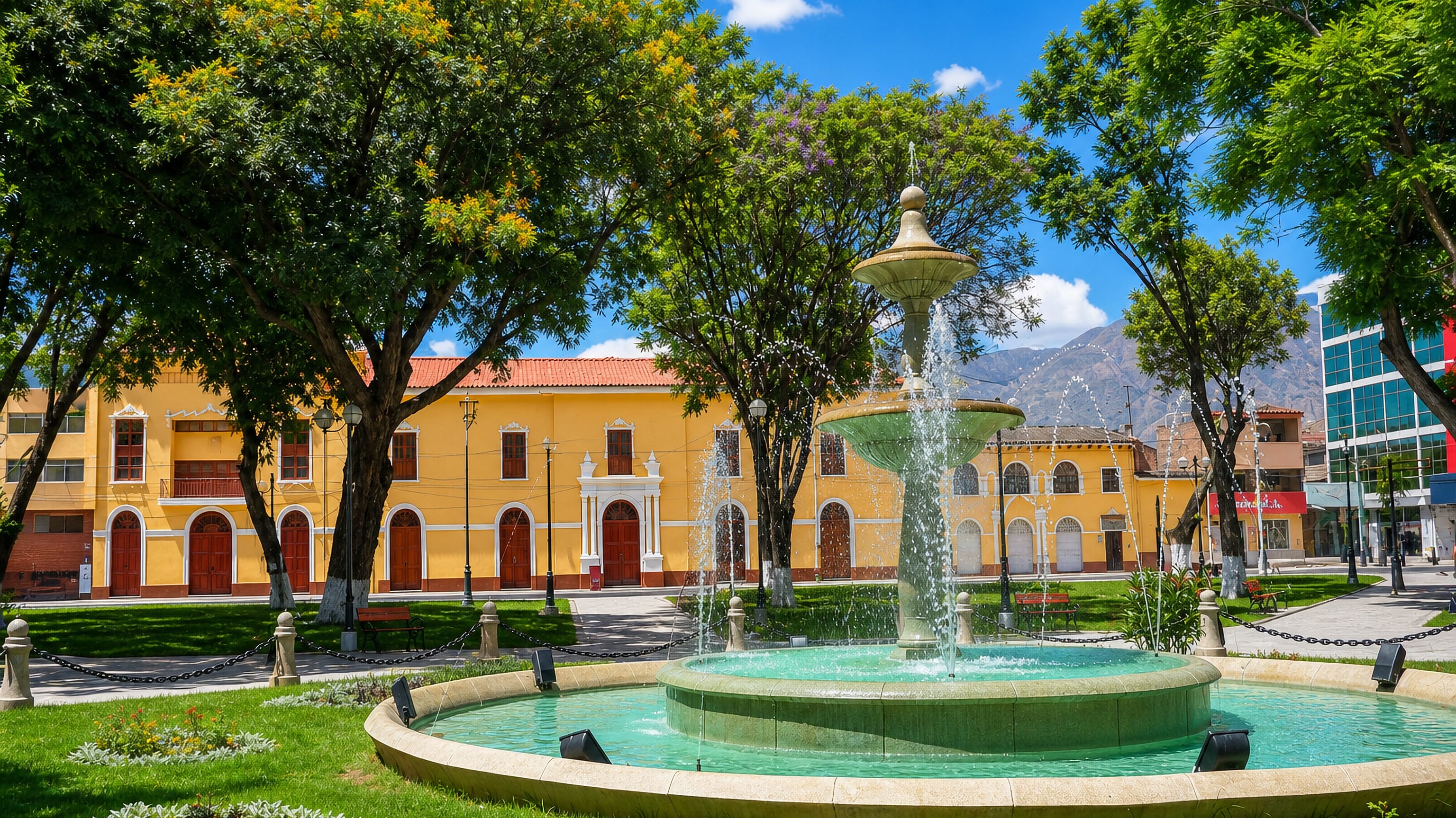 Fountain and yellow colonial arcades on Huanuco's Plaza de Armas, with Andean ridges rising behind.