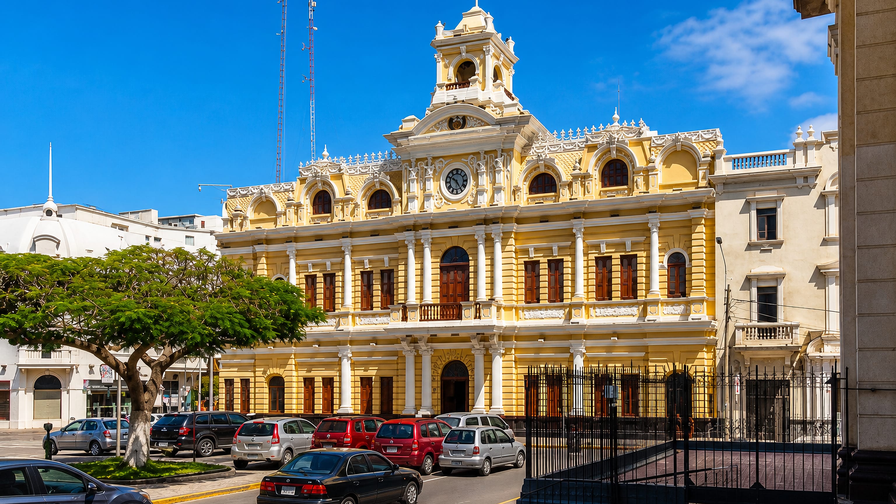 The yellow neoclassical Palacio Municipal with its clock tower on a sunlit street in central Chiclayo, Peru.