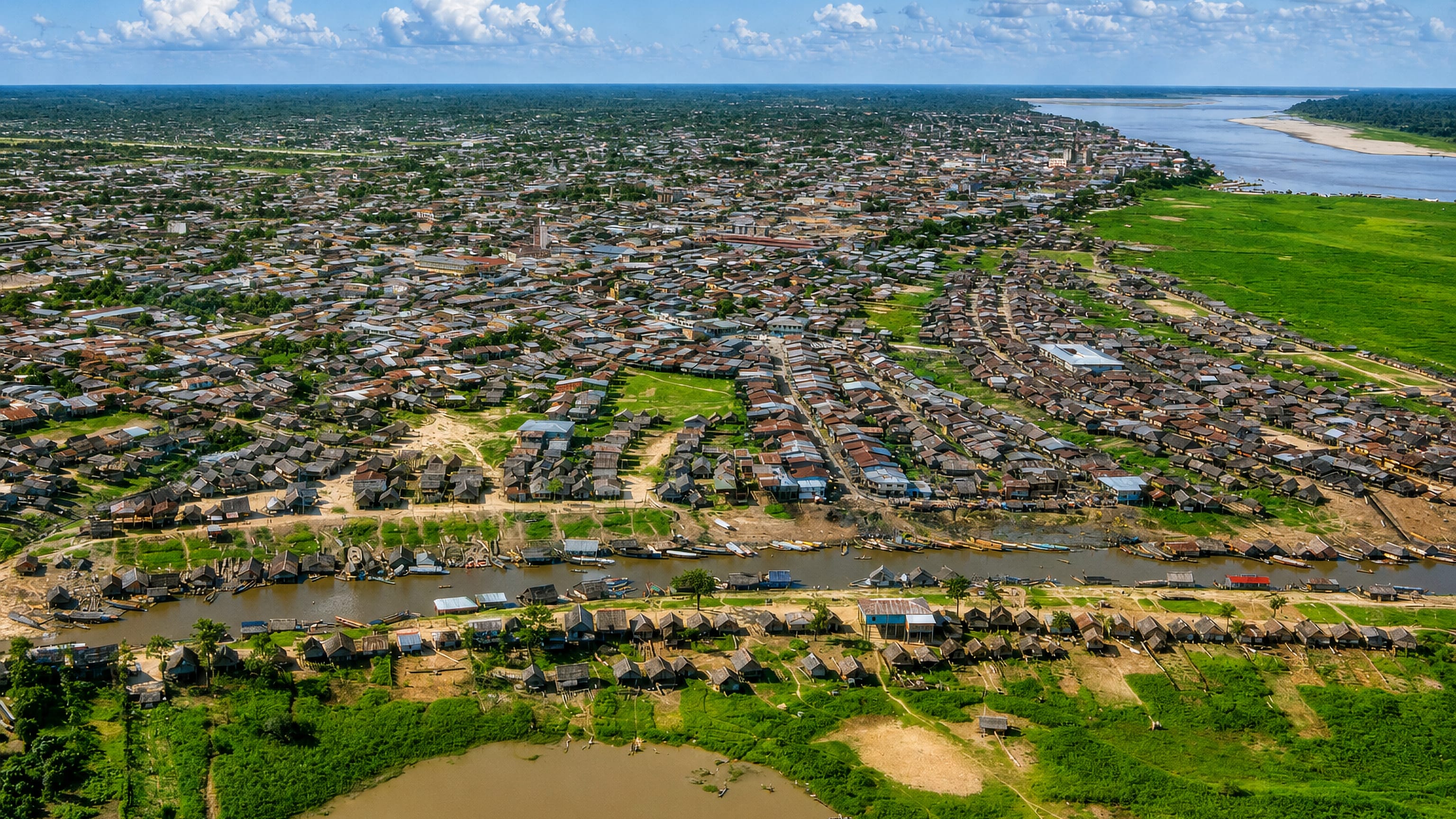 Aerial view of Iquitos, Peru, with stilt houses and boats along the river channel at the Amazon's edge.