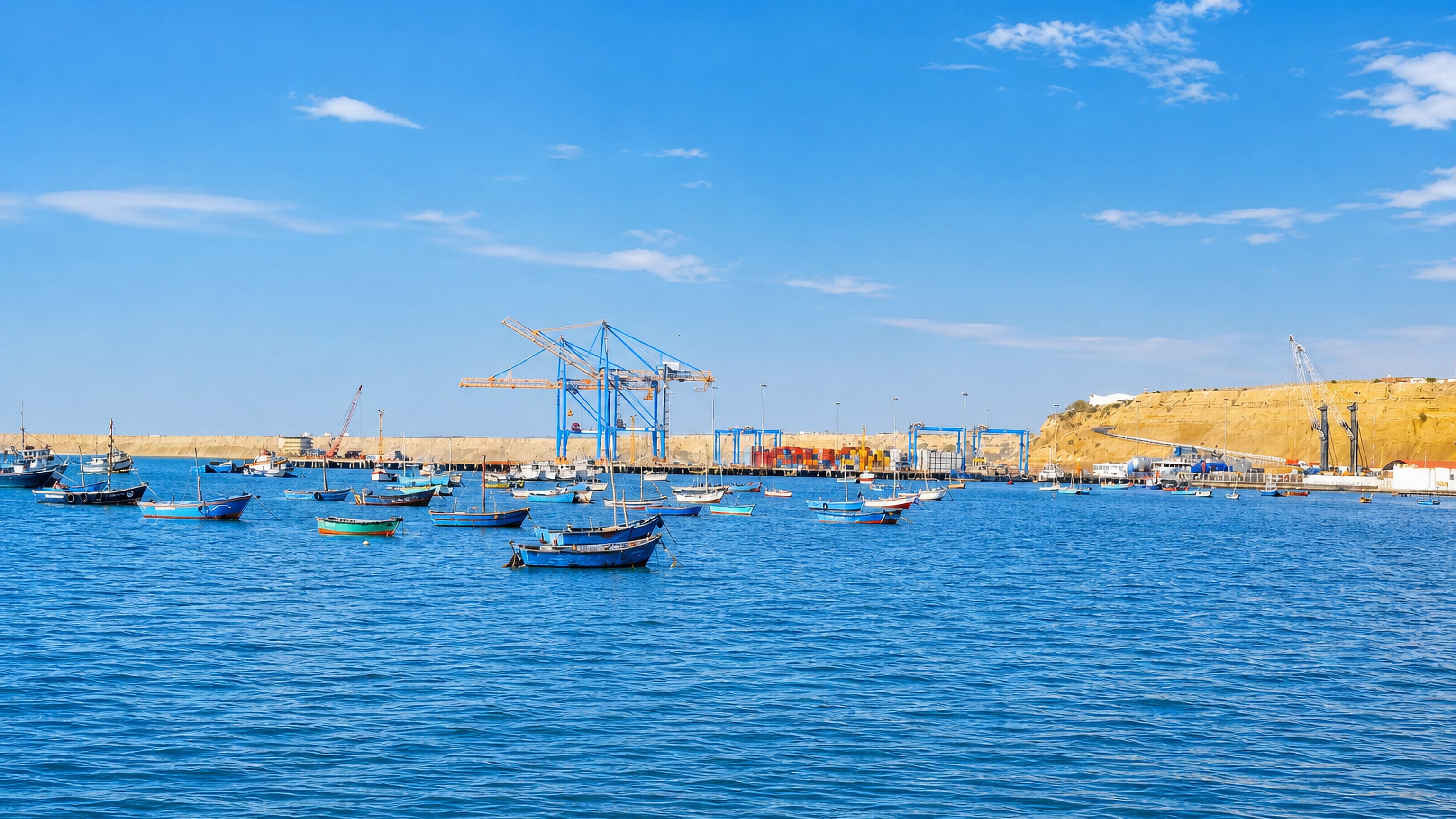 Fishing boats moored off Paita, Peru, with container cranes and the desert bluff behind the port