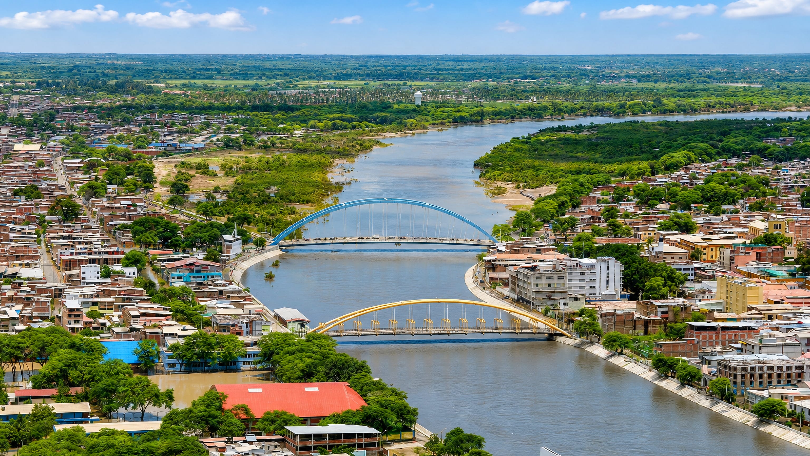 Aerial view of Piura, Peru, split by the Piura River with its blue and yellow arch bridges.