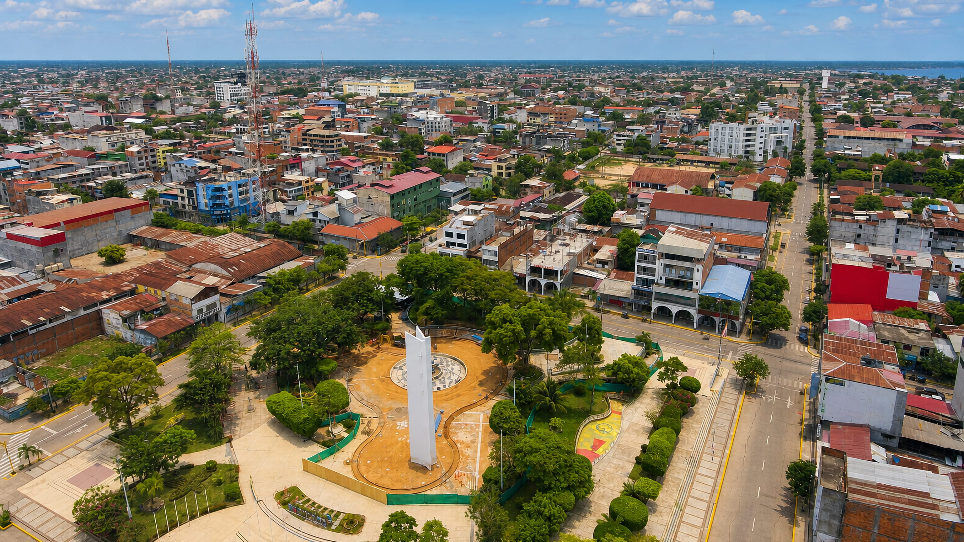 Aerial view over Pucallpa's tree-lined central plaza and obelisk, with the Ucayali waterway on the horizon
