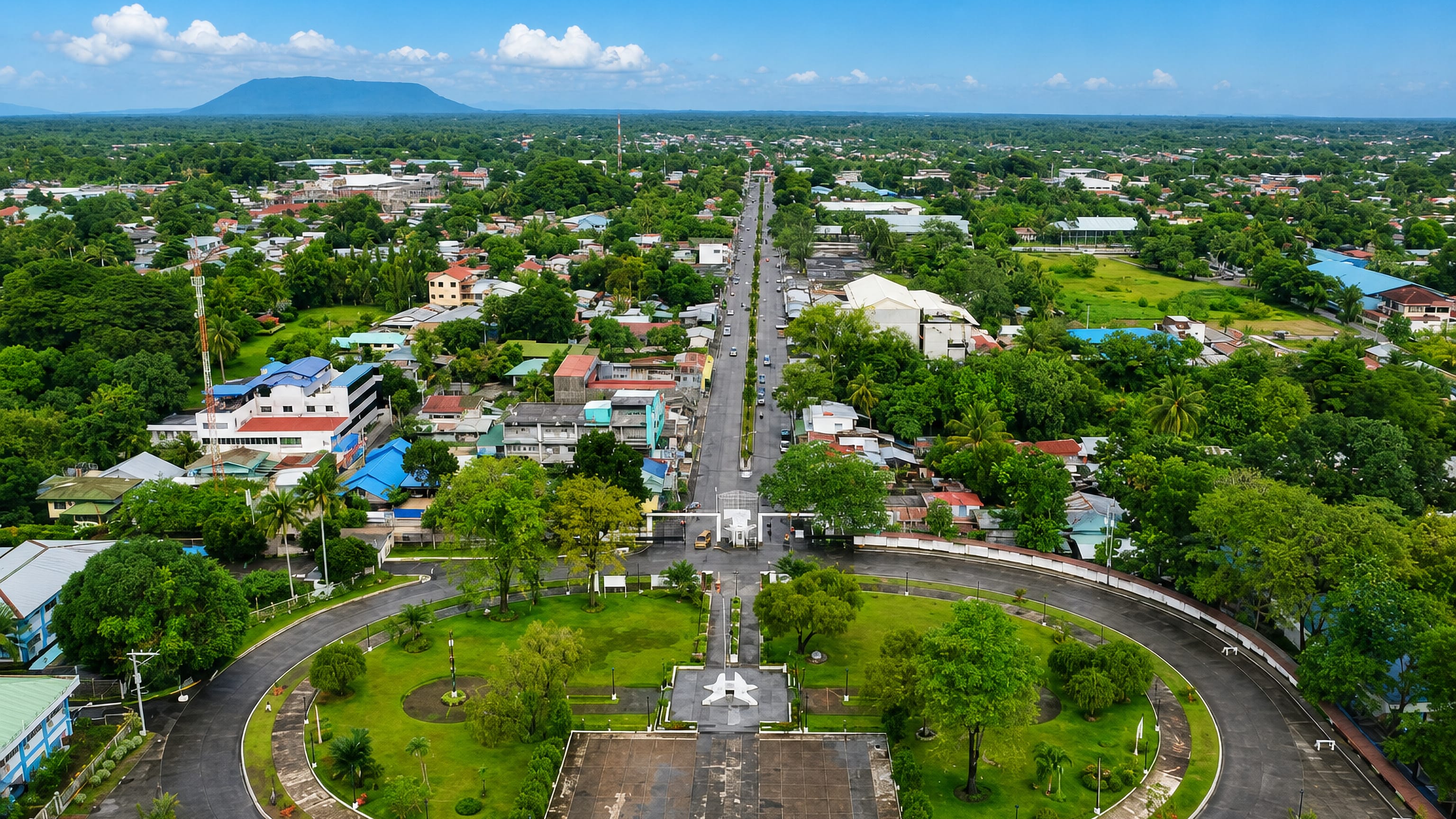 Aerial view of Cotabato's oval plaza and tree-lined main avenue with a distant mountain ridge.