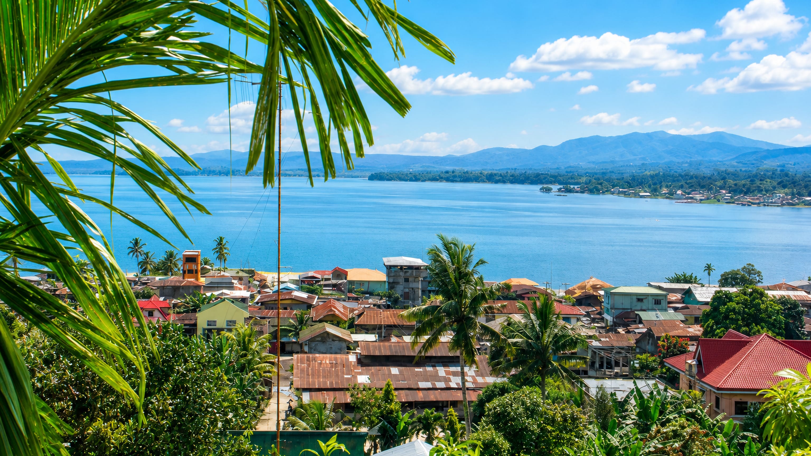 Rusted-roof houses of Marawi City rising above the shore of Lake Lanao with forested mountains beyond.