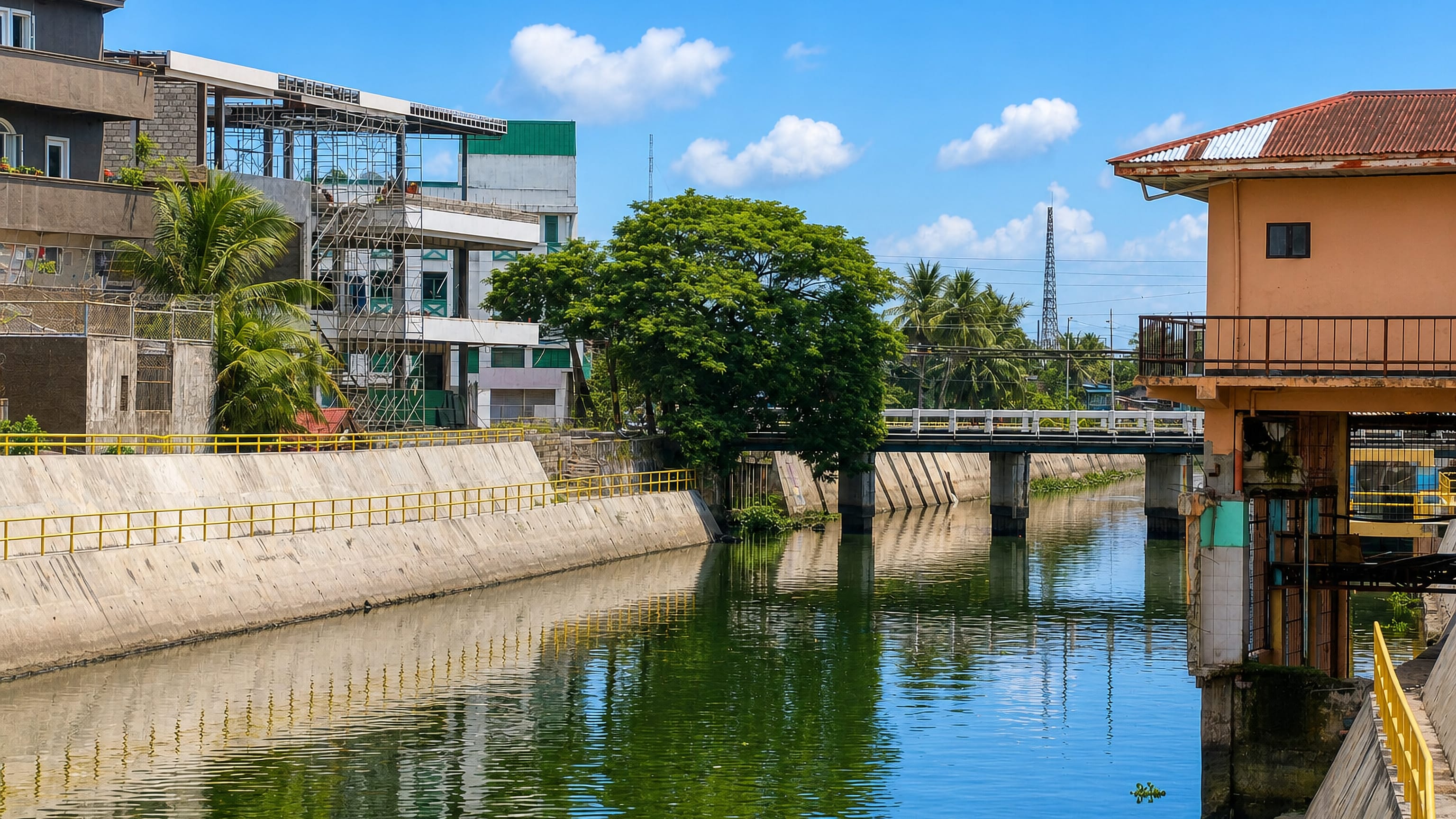 Concrete-walled river channel and low bridge running past mixed buildings in Naga, Philippines.