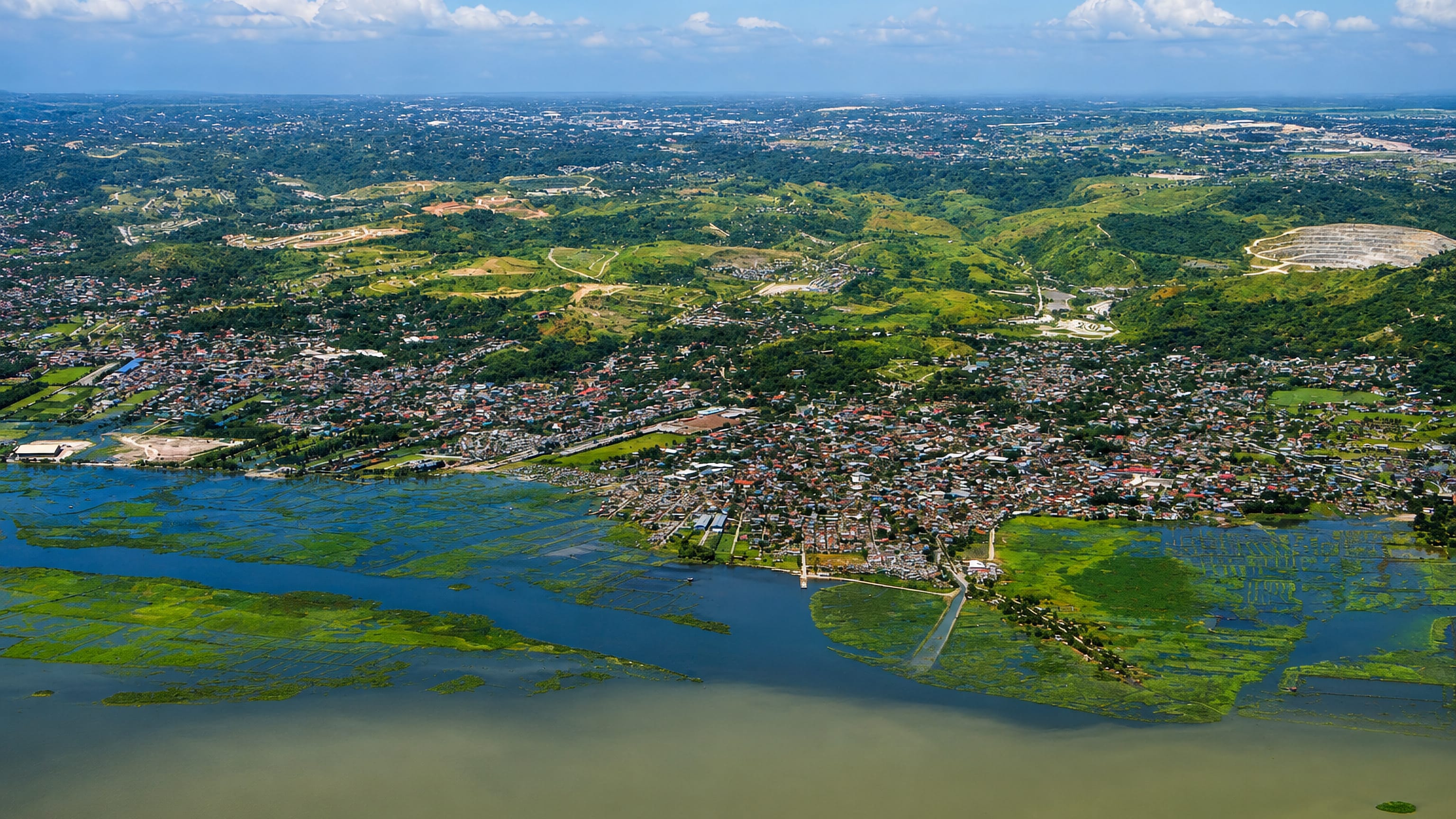 Aerial view of Angono, Philippines, on the shore of Laguna de Bay with fish pens, green hills and a quarry.