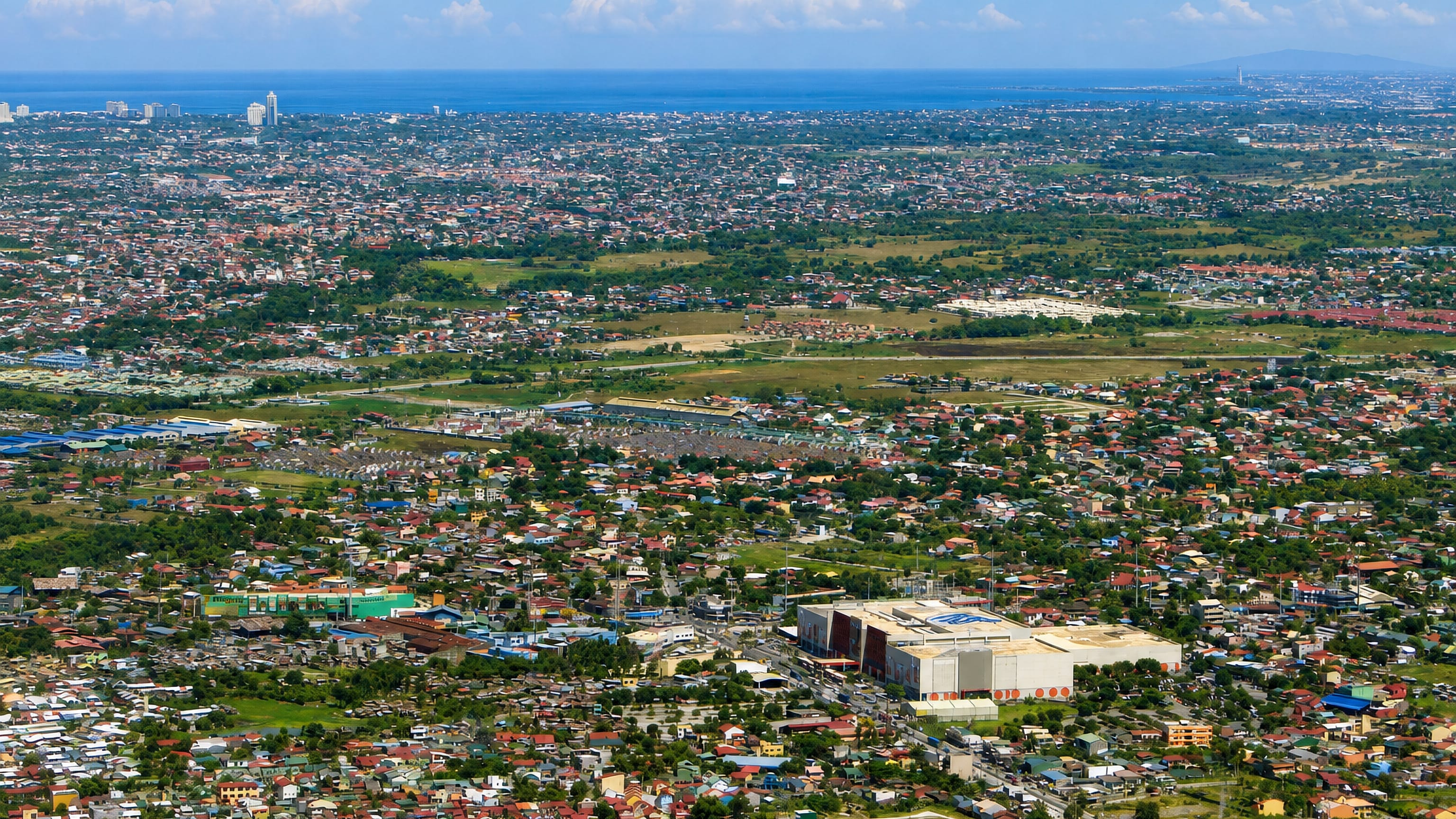 Aerial sweep over Bacoor's dense low-rise sprawl in Cavite, stretching out to Manila Bay on the horizon.