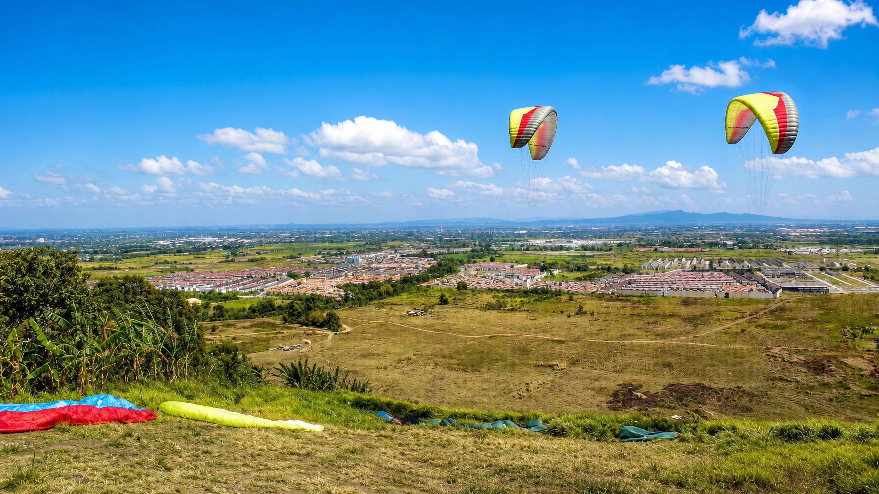 Paragliders above the grassy ridge over Carmona, Philippines, with housing subdivisions on the plain.