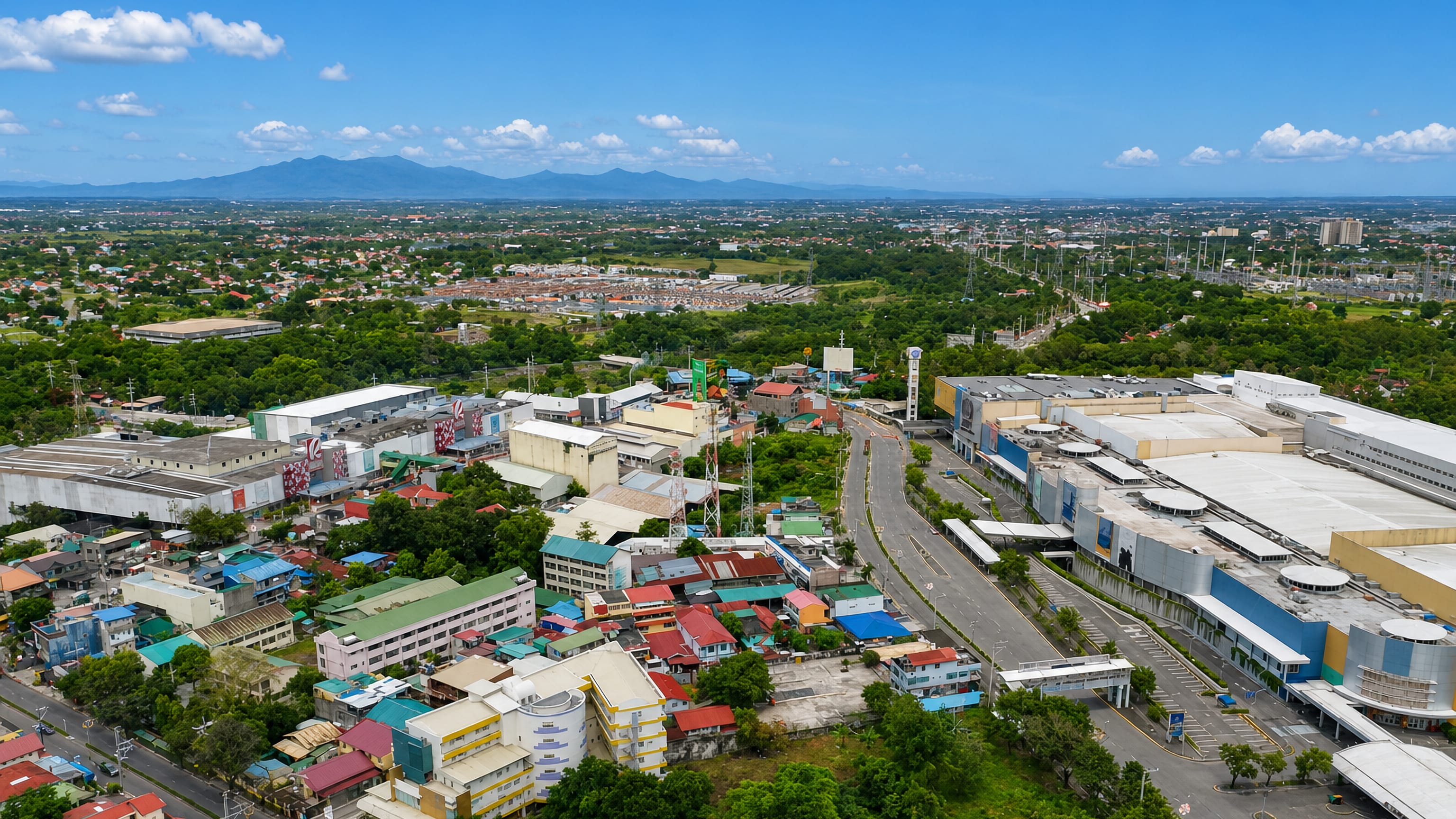 Aerial view of Dasmariñas, Cavite, with a shopping mall, low-rise streets and mountains on the horizon.