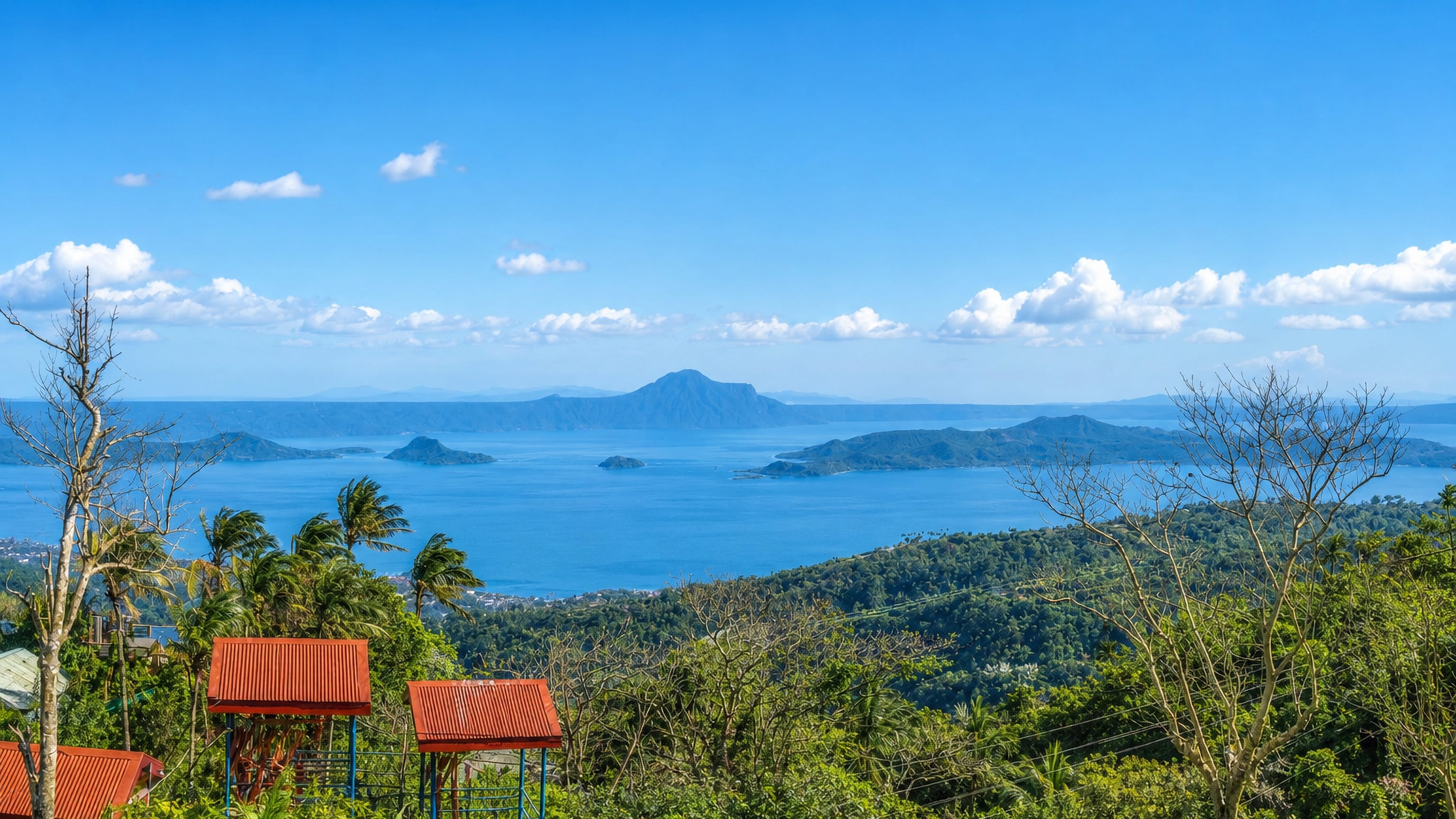 Taal Lake and its volcano island seen from the ridge at Tagaytay, Philippines, with red-roofed viewing huts.