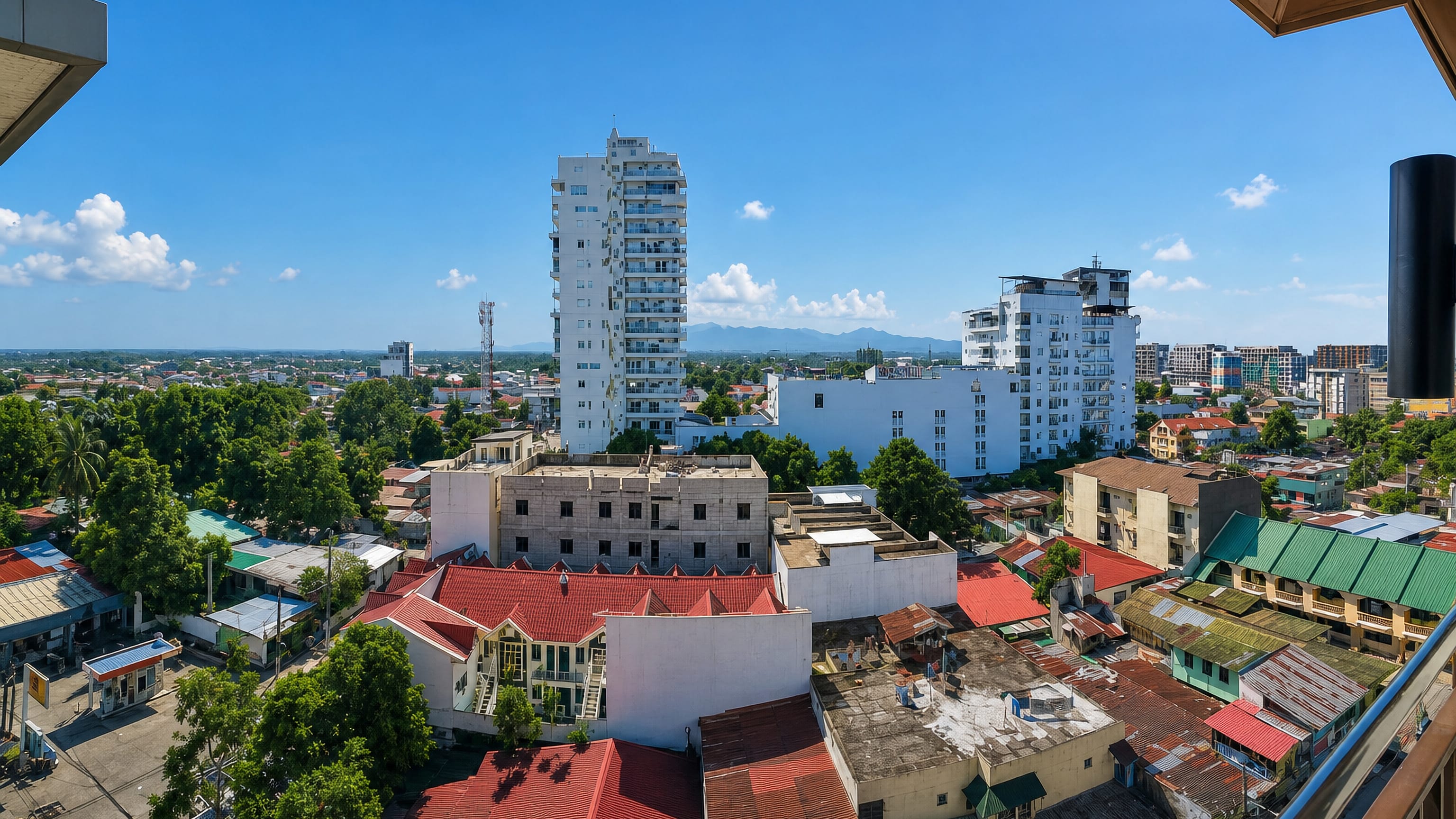 Rooftop view across Angeles City's red-roofed houses and mid-rise towers toward distant mountains in Central Luzon.