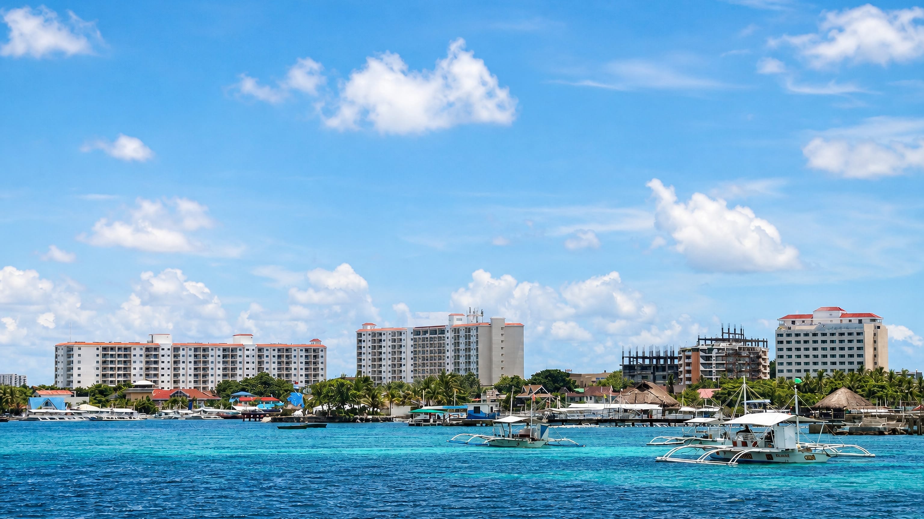 Turquoise water, outrigger boats and beachfront resort towers at Lapu-Lapu City, Philippines