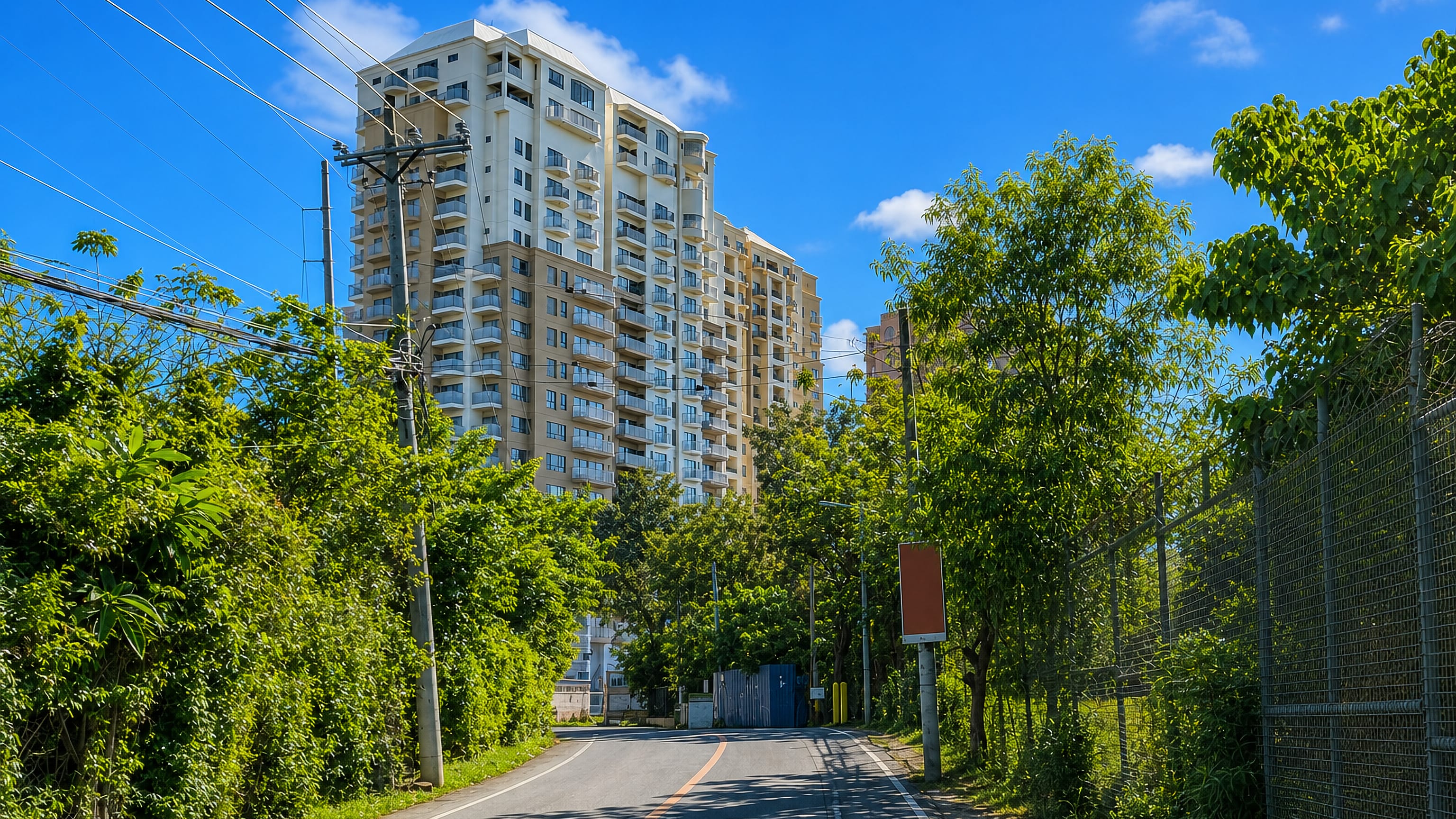 Tree-lined road curving toward a high-rise condominium tower under blue sky in Punta Engaño, Lapu-Lapu City.