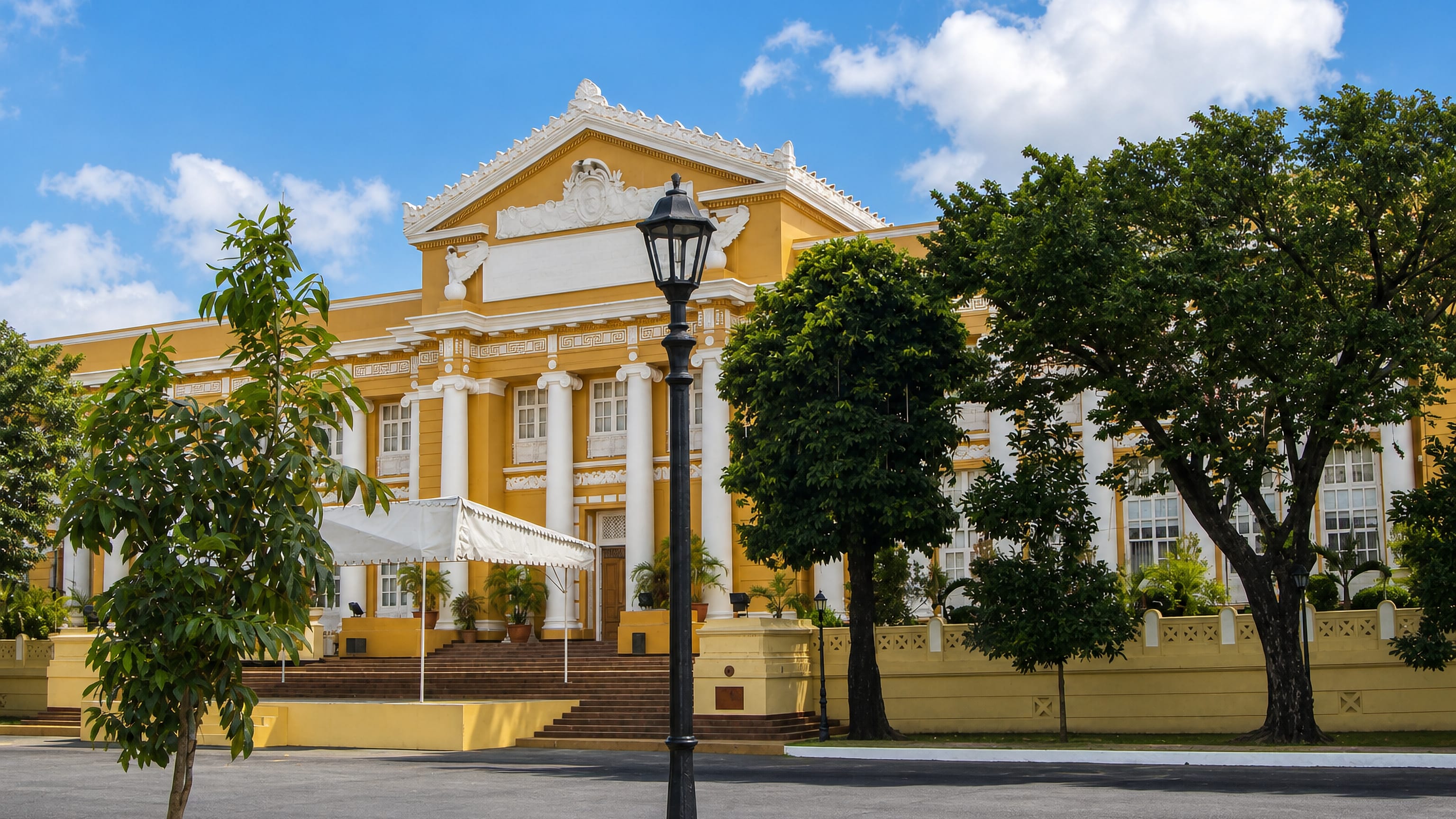 The yellow neoclassical Pangasinan Provincial Capitol behind palms and a street lamp in Lingayen, Philippines.