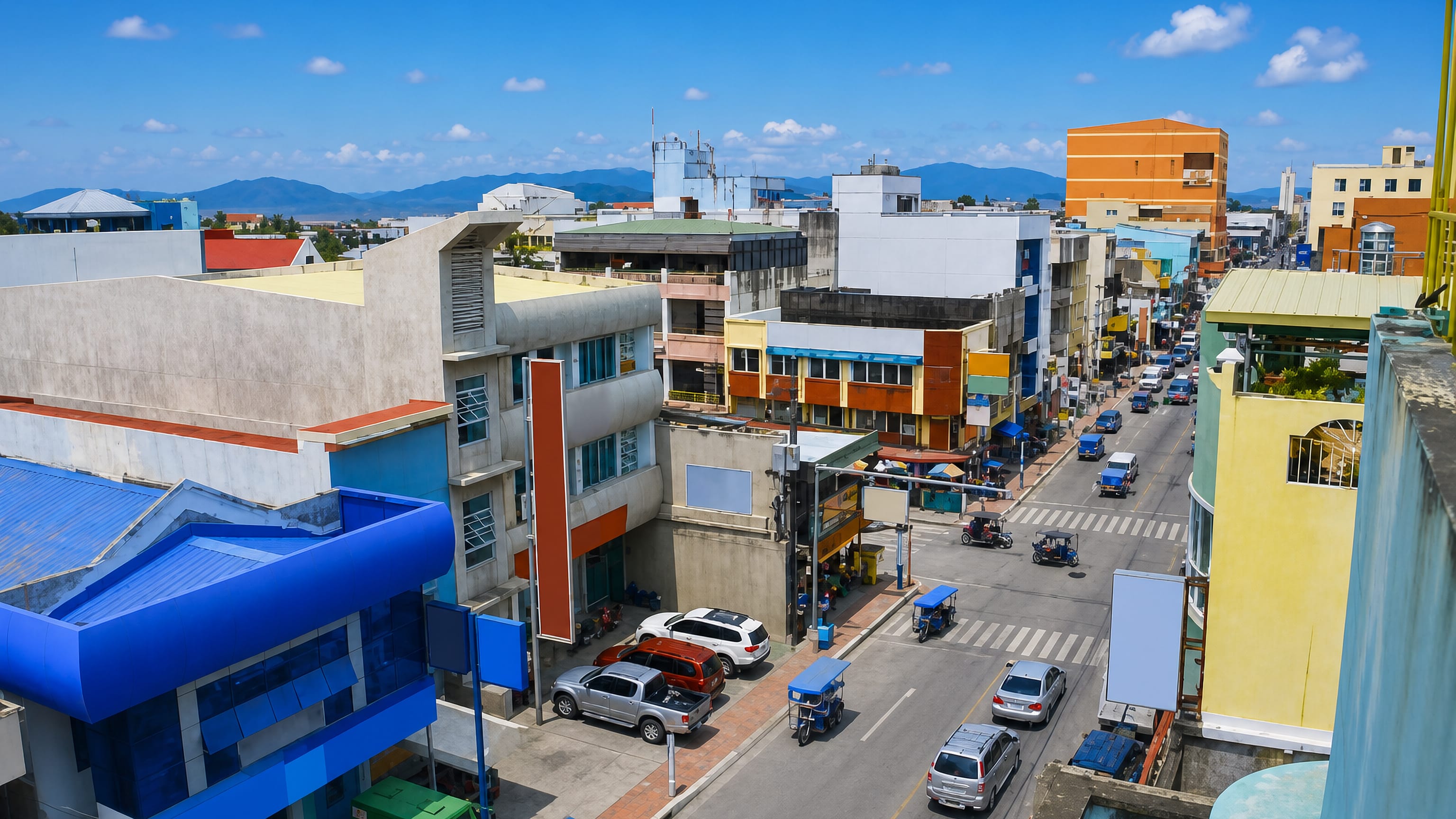 Rooftop view over Calapan, Philippines, with colourful low-rise shops, tricycles and Mindoro's mountains.