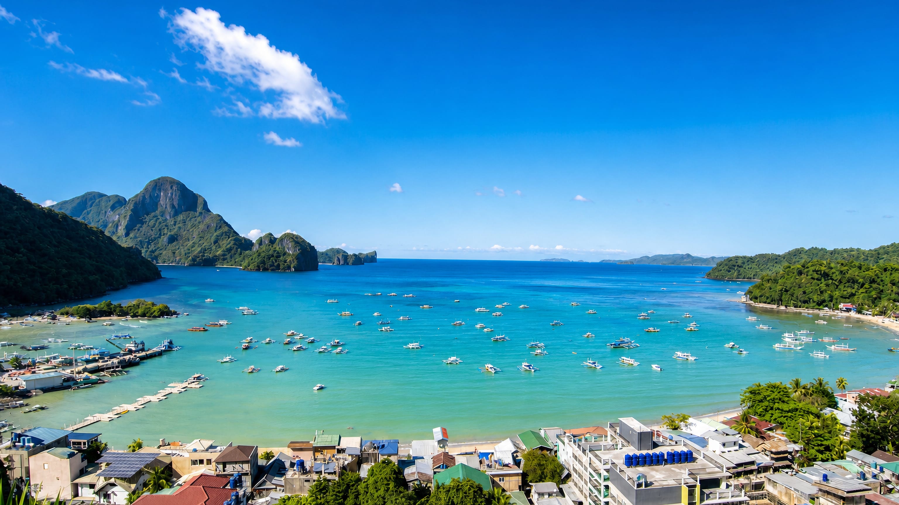 El Nido's rooftops above Bacuit Bay, outrigger boats moored below Palawan's limestone karst cliffs.