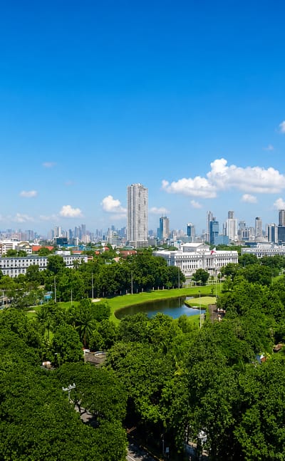 Green parkland and a golf course in front of Manila's mid-rise skyline under a bright blue sky