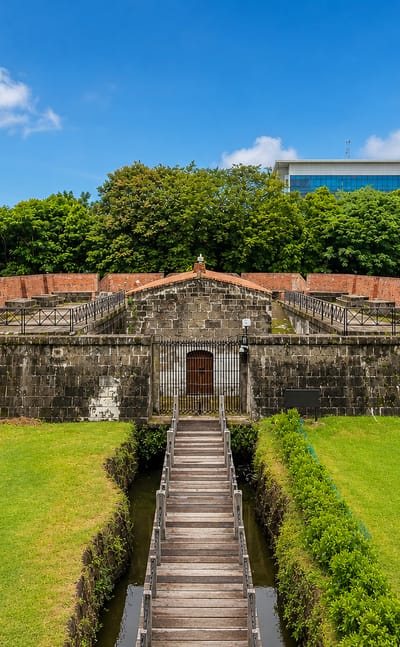Stone and brick ramparts of Intramuros, Manila, reached by a wooden footbridge over a moat.