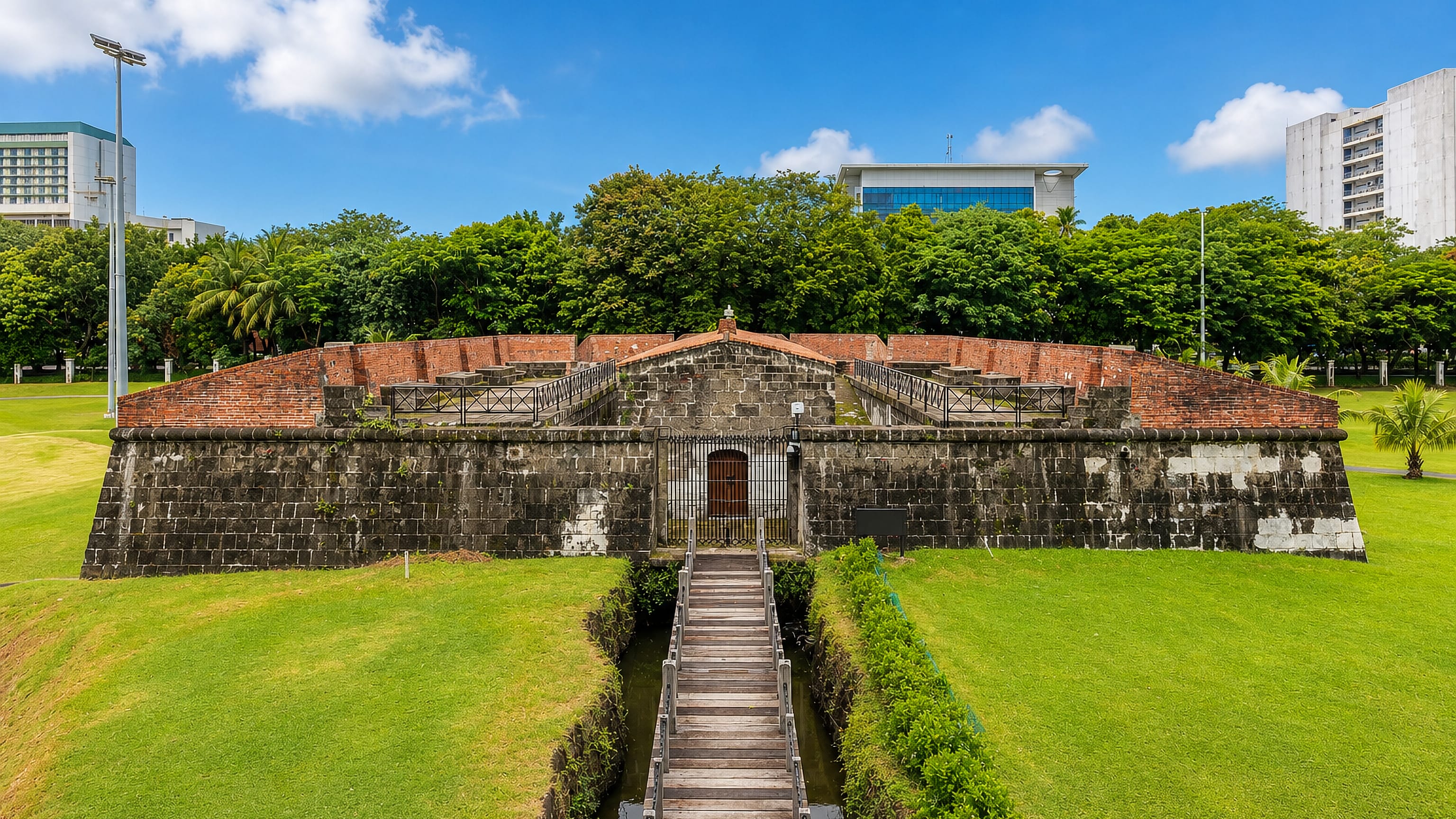 Stone and brick ramparts of Intramuros, Manila, reached by a wooden footbridge over a moat.