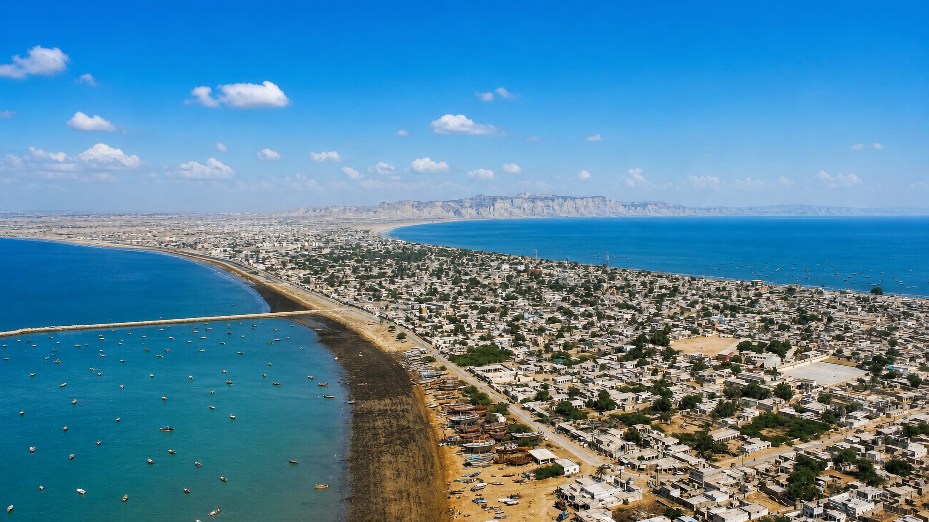 Gwadar spread along its sandy isthmus between two bays, with fishing boats and coastal cliffs, Balochistan.