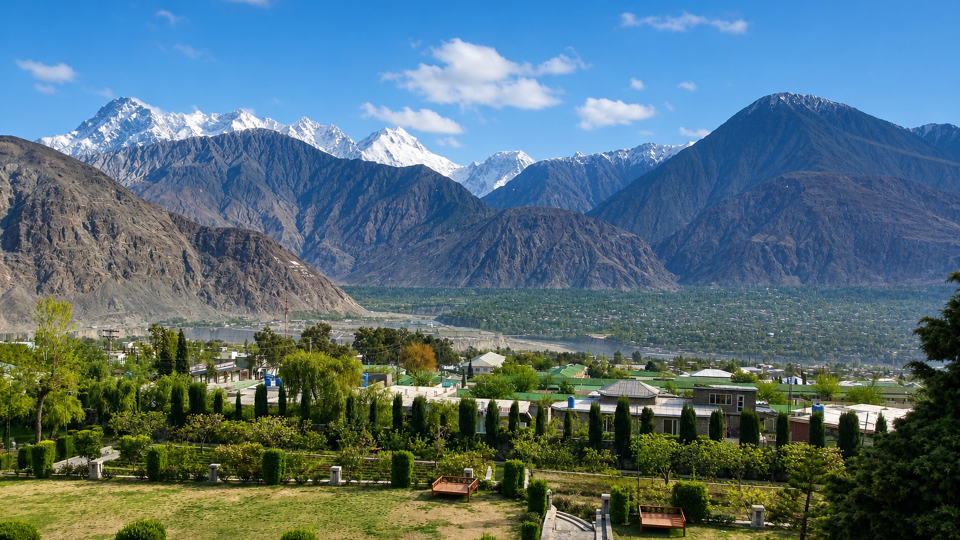 Gilgit, Pakistan, in its river valley with gardens in the foreground and snow-capped Karakoram peaks beyond.