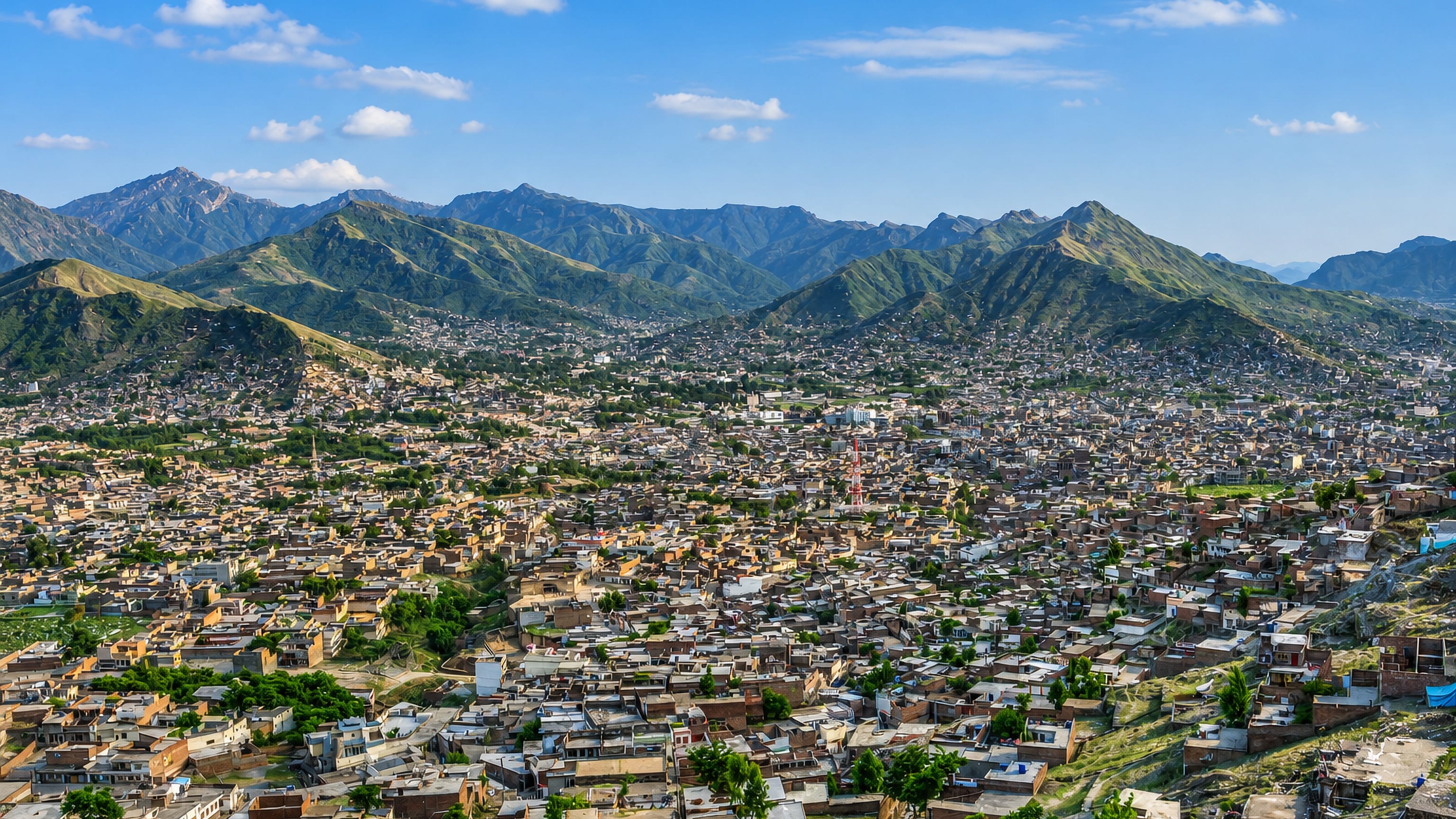 Dense rooftops of Mingora filling the Swat valley floor beneath green mountain ridges in Pakistan.