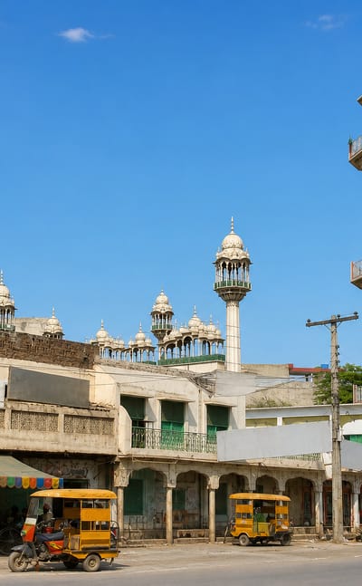 Street corner in Daska, Sialkot district, with a brick mosque minaret above arcaded shops and rickshaws.