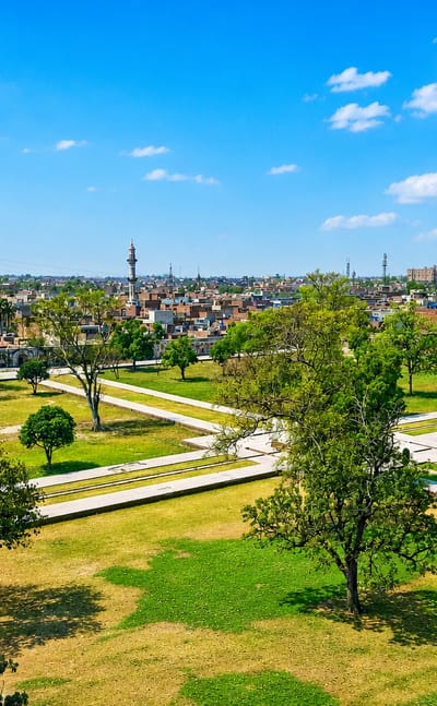 Wide daytime view over Lahore rooftops and distant minarets seen from a green park with trees and pathways.