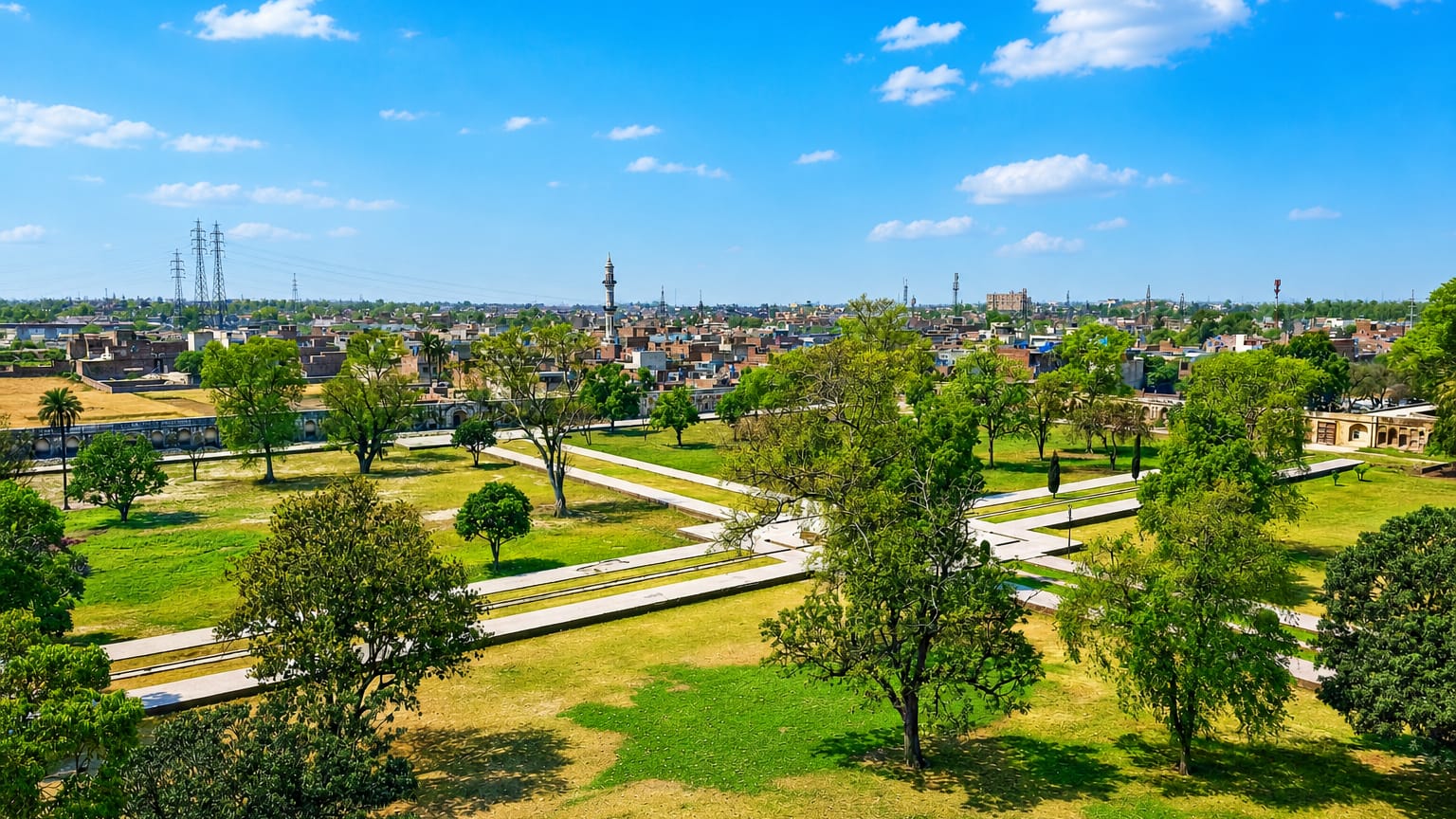 Wide daytime view over Lahore rooftops and distant minarets seen from a green park with trees and pathways.