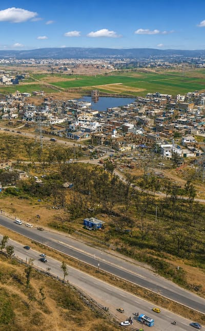 Aerial view of Rawalpindi's outskirts, a highway between scattered houses, fields and distant hills, Pakistan.
