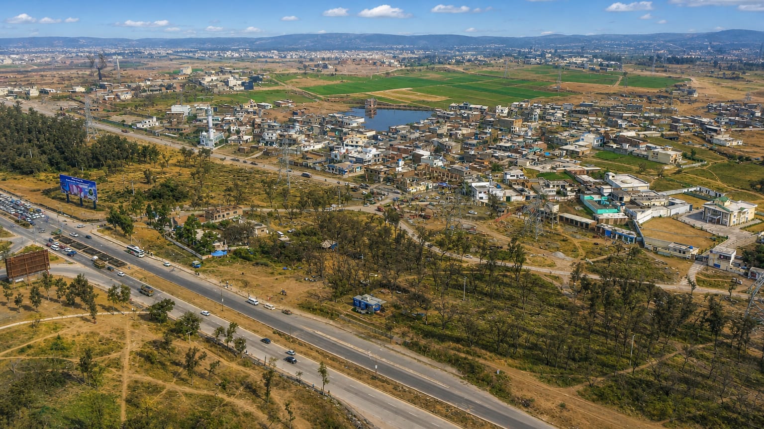 Aerial view of Rawalpindi's outskirts, a highway between scattered houses, fields and distant hills, Pakistan.