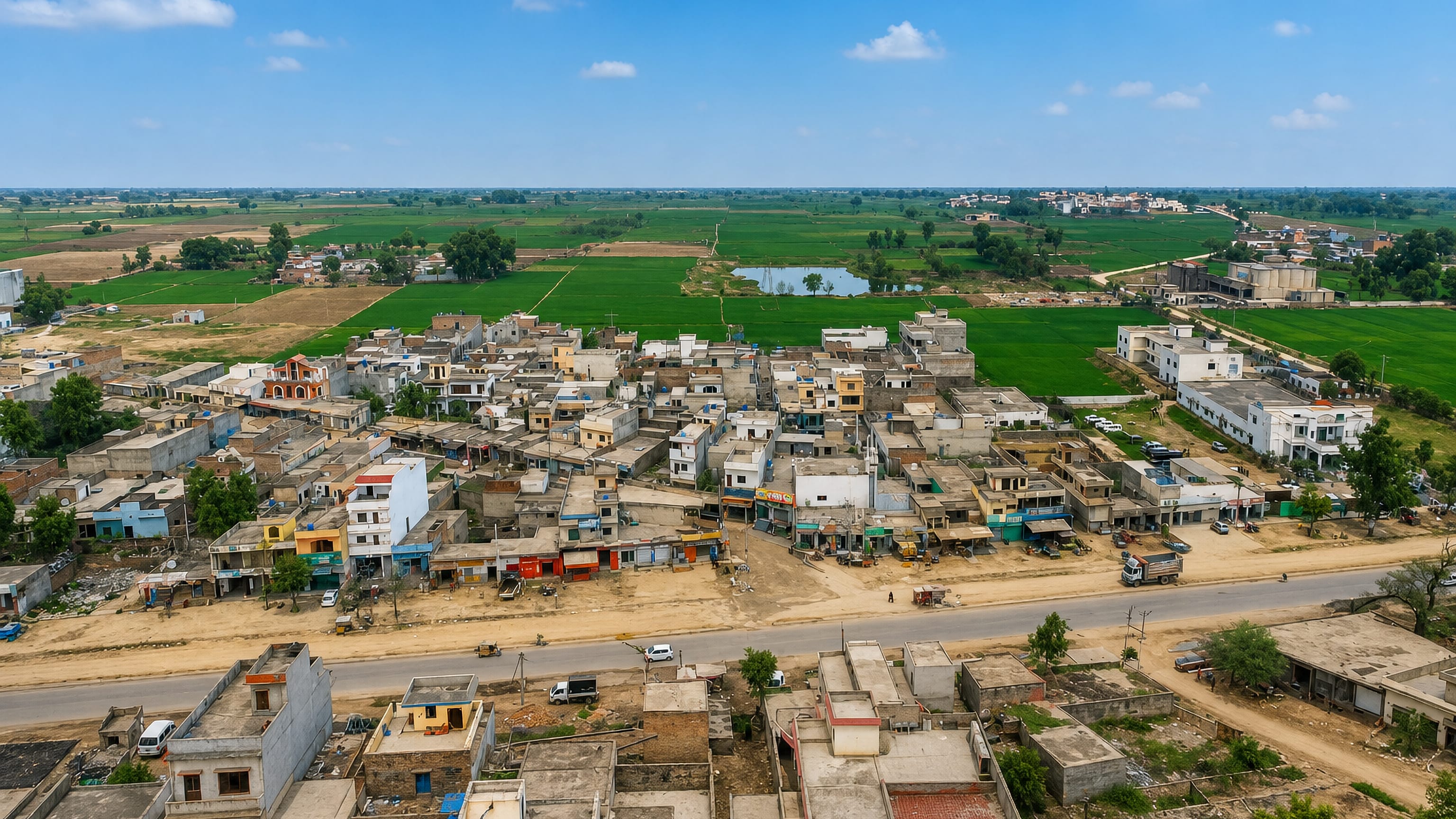 Aerial view of Wazirabad, Punjab, with flat-roofed houses along a main road and green farmland beyond.